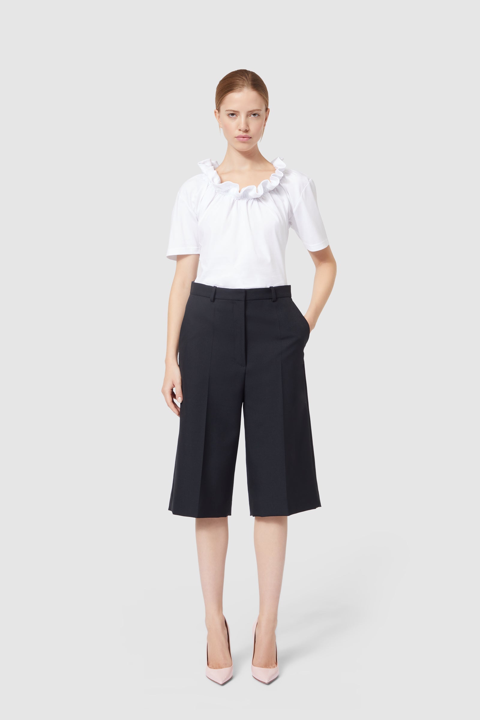 Elegant outfit featuring a ruffled white blouse paired with tailored black culottes, complemented by sleek pink heels.
