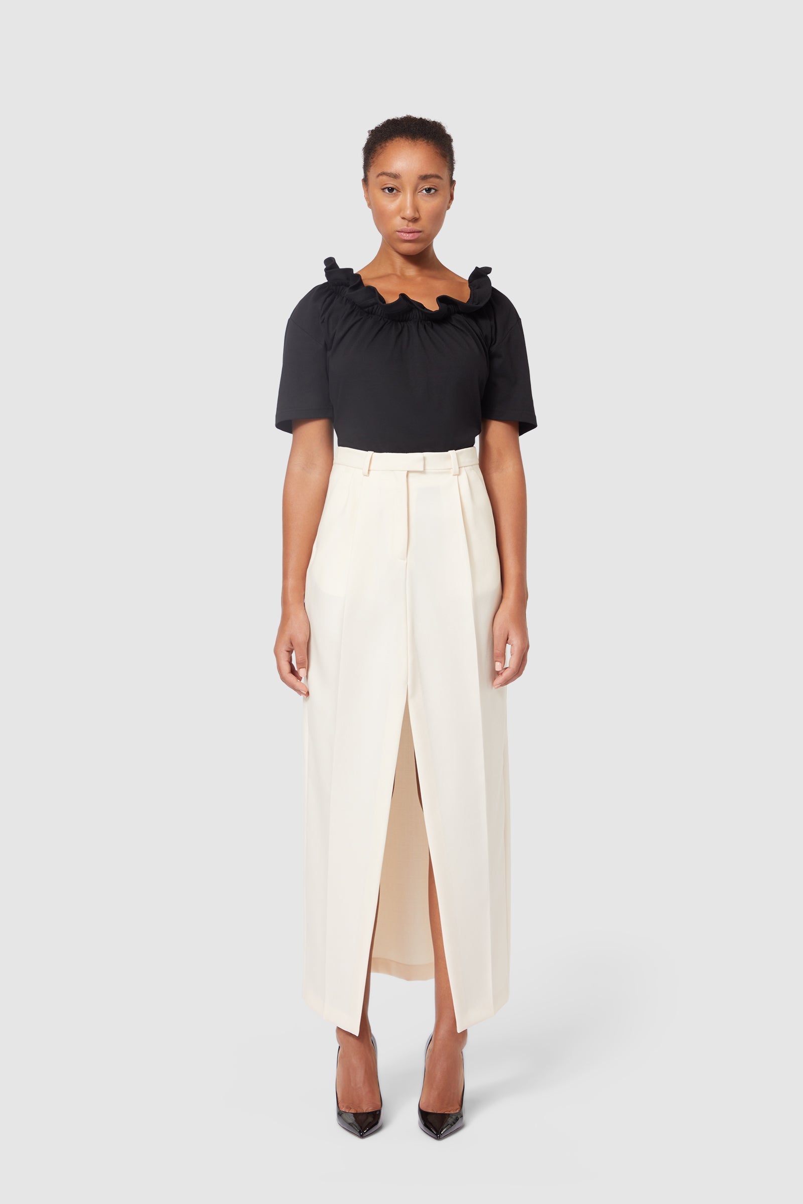 Elegant ensemble featuring a black ruffled neckline blouse paired with a high-waisted off-white maxi skirt slit.