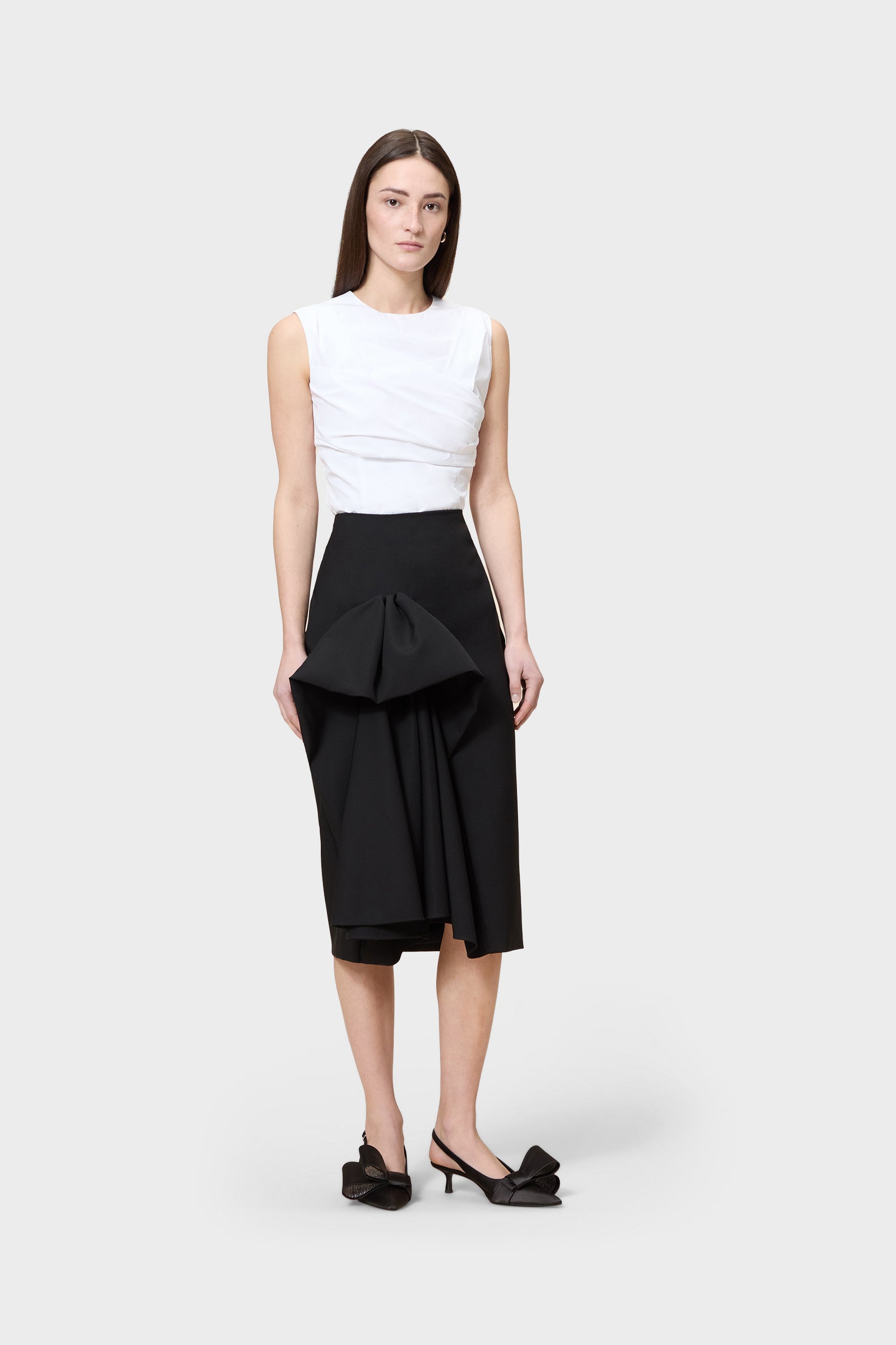 Model wearing a white top with a black skirt on a white background.