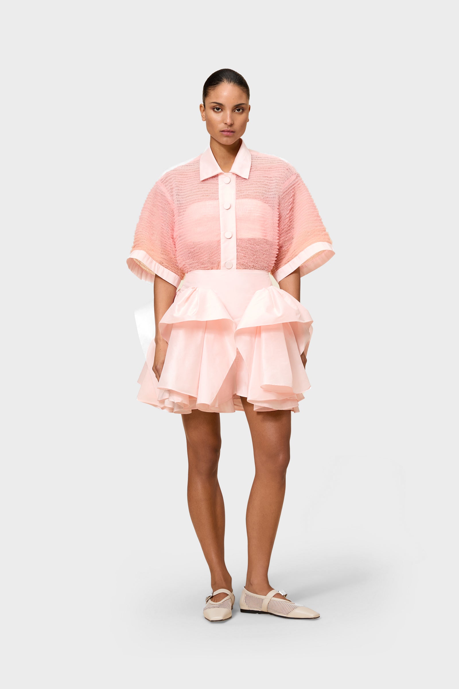 Pink tulle shirt with pink ruffled skirt on a white background worn by a model.