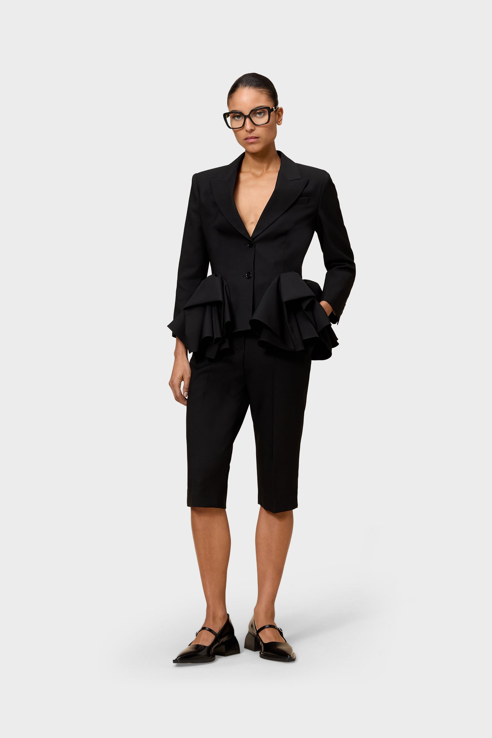 Model wearing a black blazer with black capri pants on a white background.