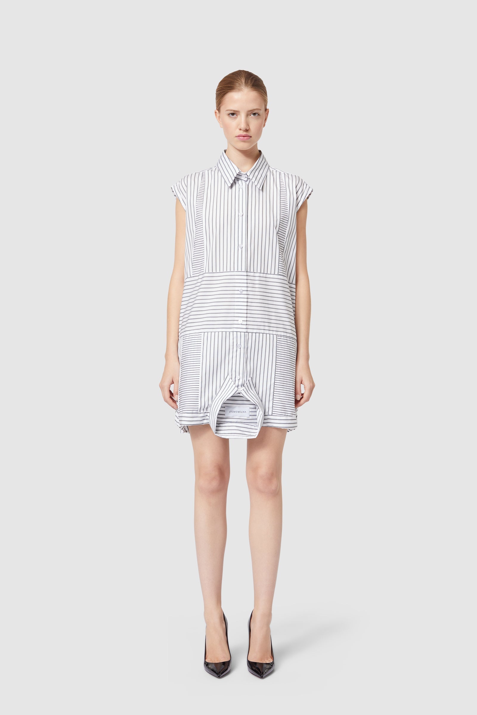 Sleeveless shirt dress with asymmetric blue and white pinstripes, featuring a button-down front and a unique hemline design.