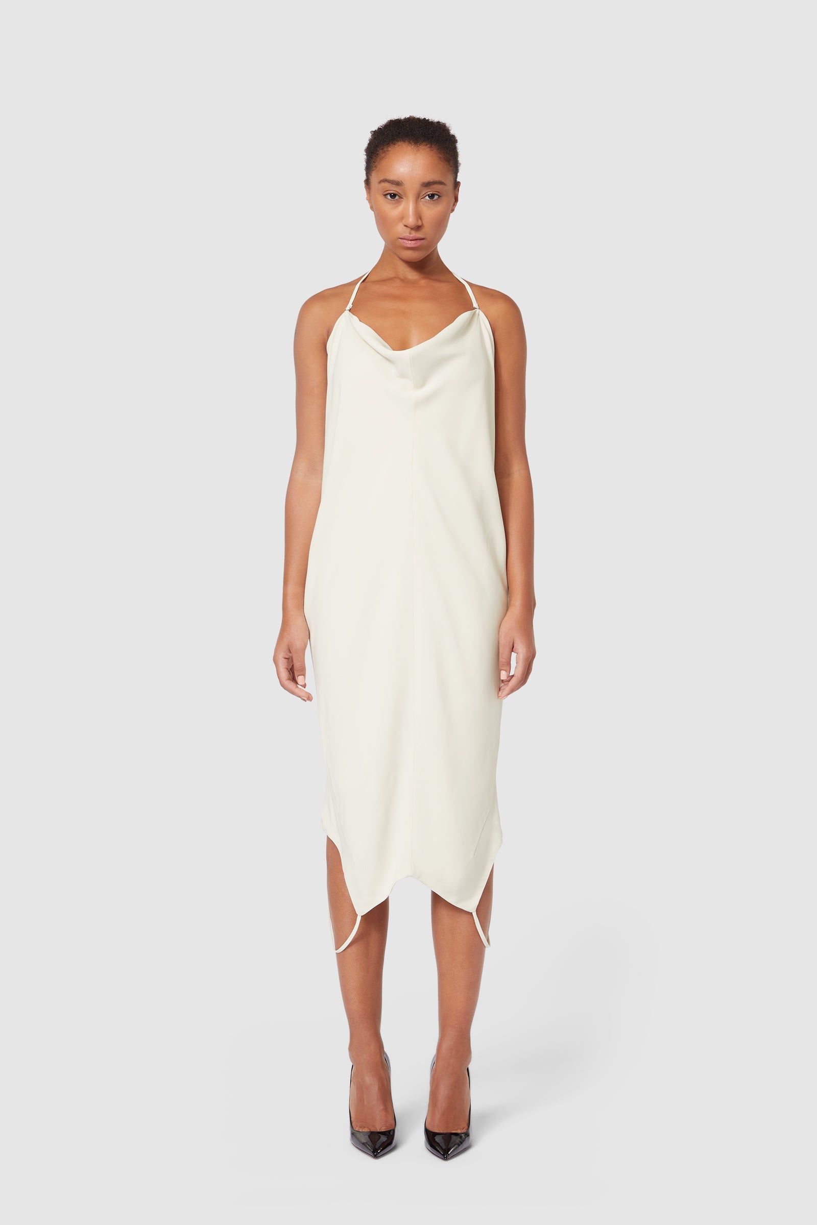 Elegant ivory slip dress with a cowl neckline, thin straps, and asymmetric hemline, creating a minimalist yet sophisticated look.
