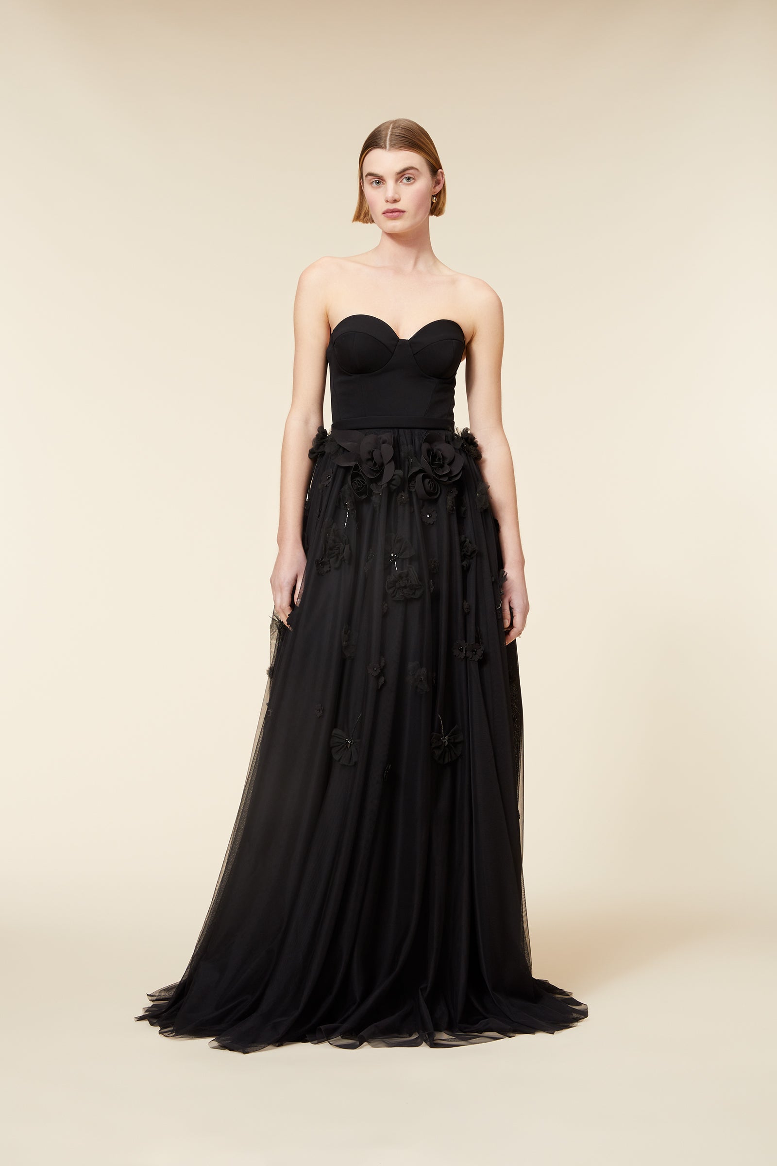 Elegant black strapless evening gown with floral appliqués and a flowing A-line skirt displayed in a minimalist setting.