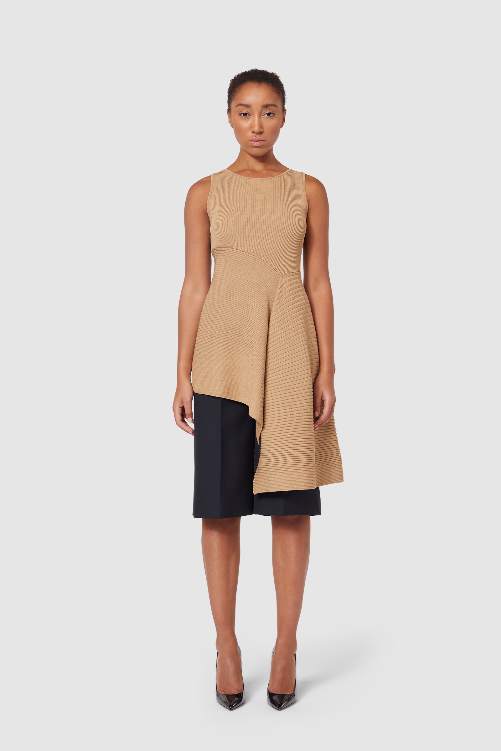 Asymmetrical tan knit top with ribbed texture, uniquely draped over tailored black shorts, creating a modern silhouette.