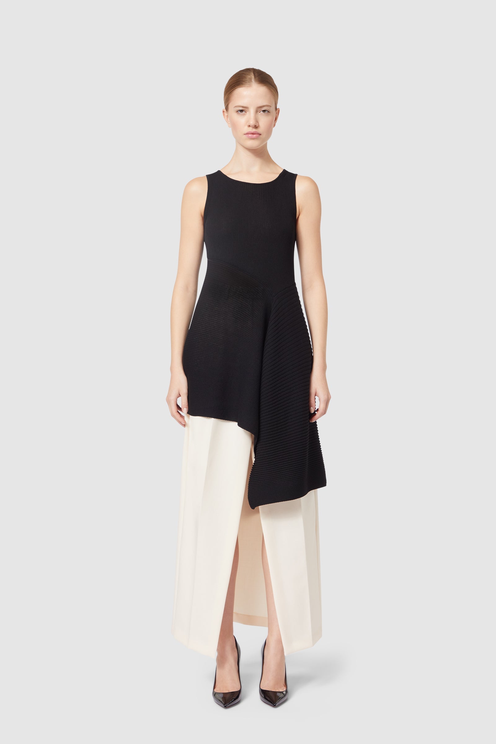 Asymmetrical black knit dress with layered cream pleated skirt, elegantly designed for a modern, sophisticated look.
