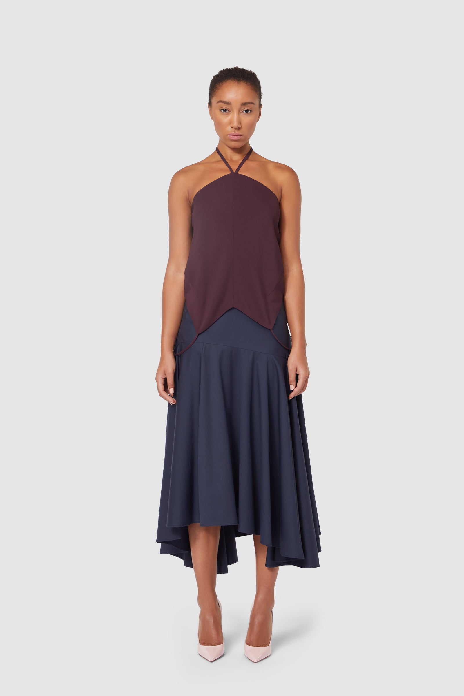 Elegant halter top with asymmetrical burgundy overlay, paired with a flowing navy-blue midi skirt and nude heels.