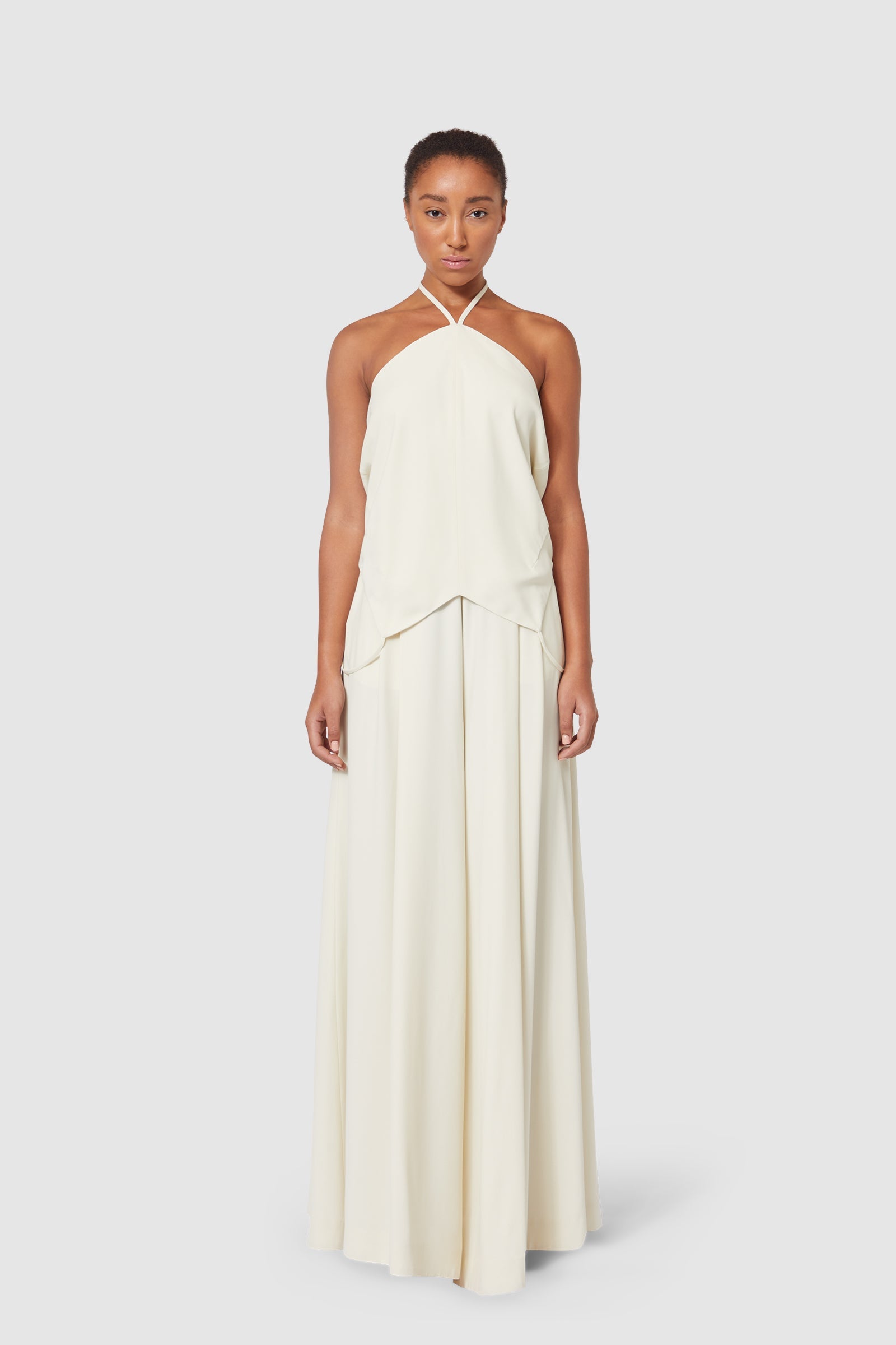 Elegant cream halter-neck dress with flowing full-length skirt, featuring subtle layered fabric detailing for a refined look.