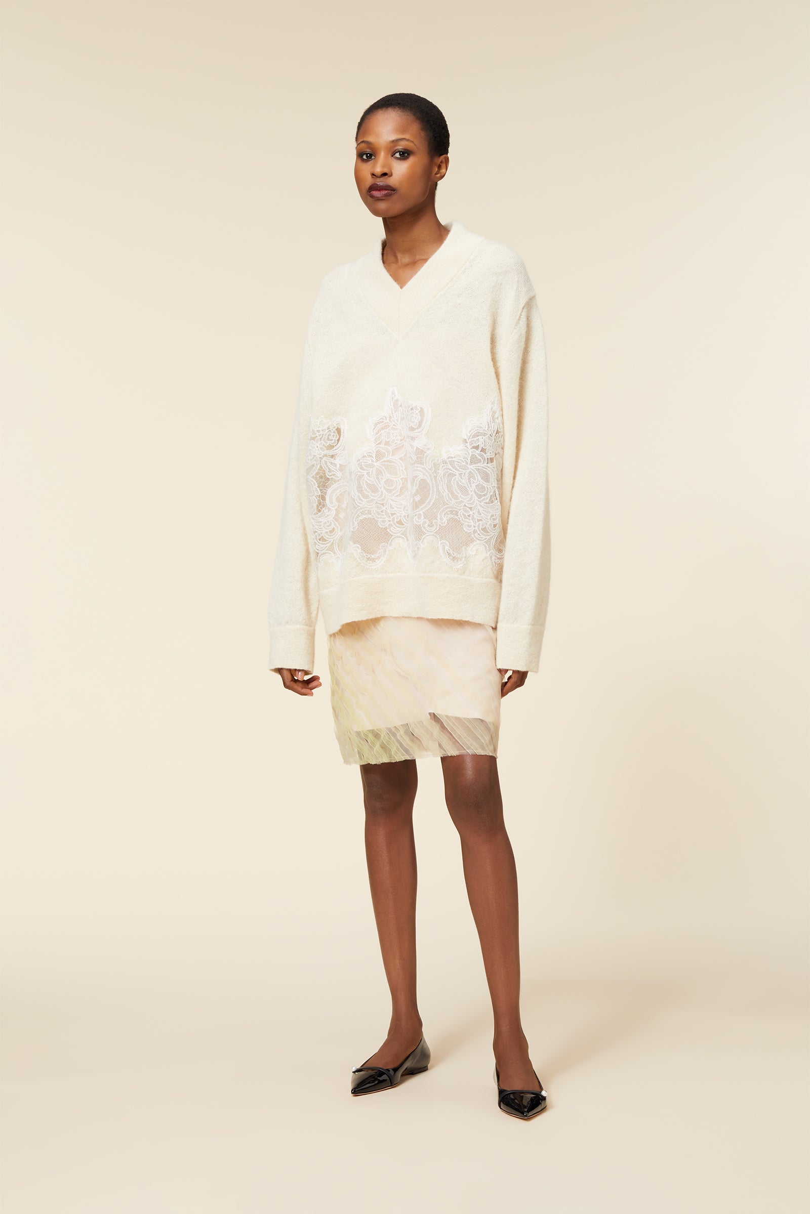Cream oversized sweater with intricate floral lace overlay paired with a delicate tulle skirt, styled with black pointed flats.