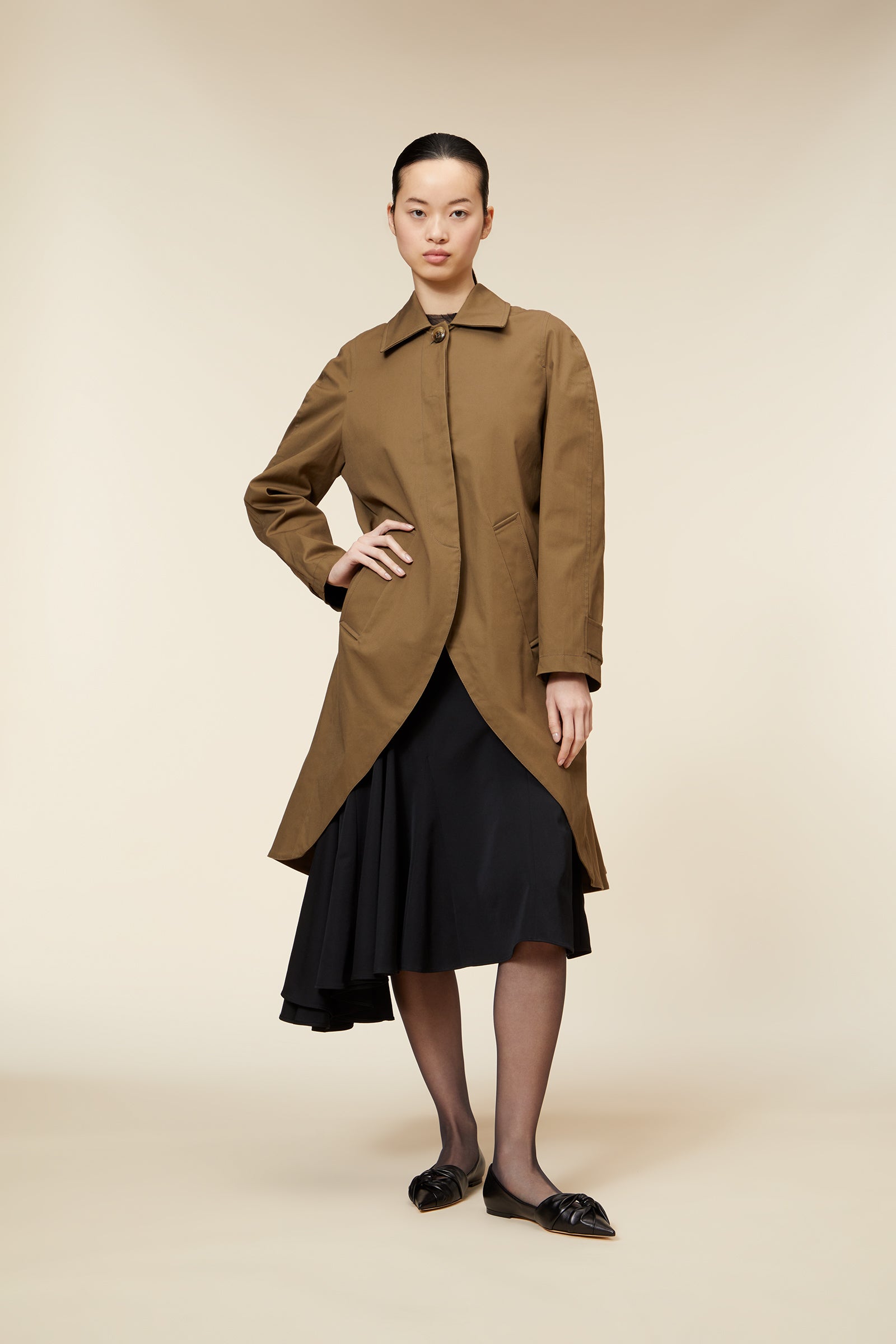 A chic camel trench coat with a classic collar, long sleeves, and tailored waist, layered over a stylish black skirt.