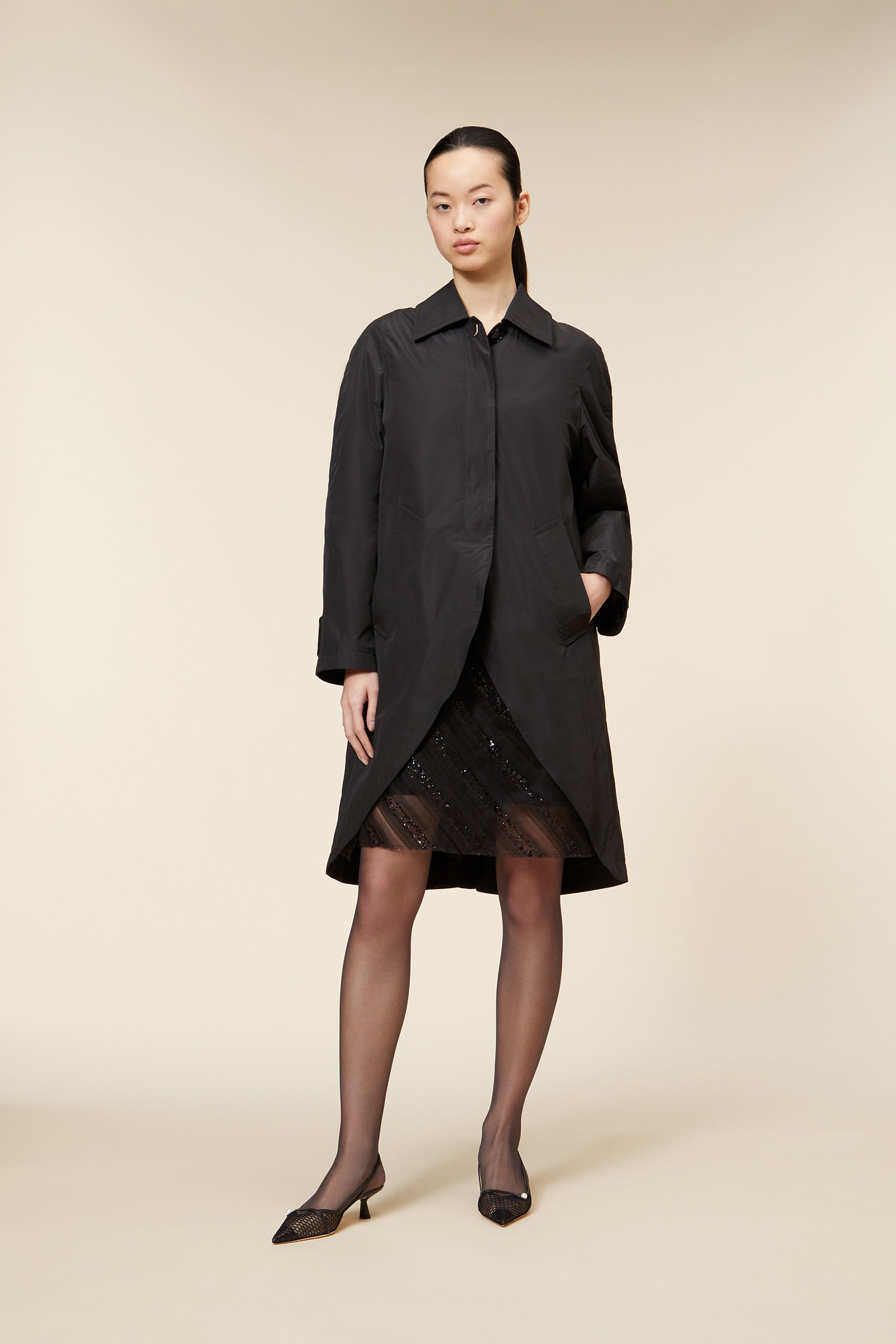 Elegant black trench coat with tailored fit, featuring subtle asymmetrical contour, paired with delicate lace detailing underneath.