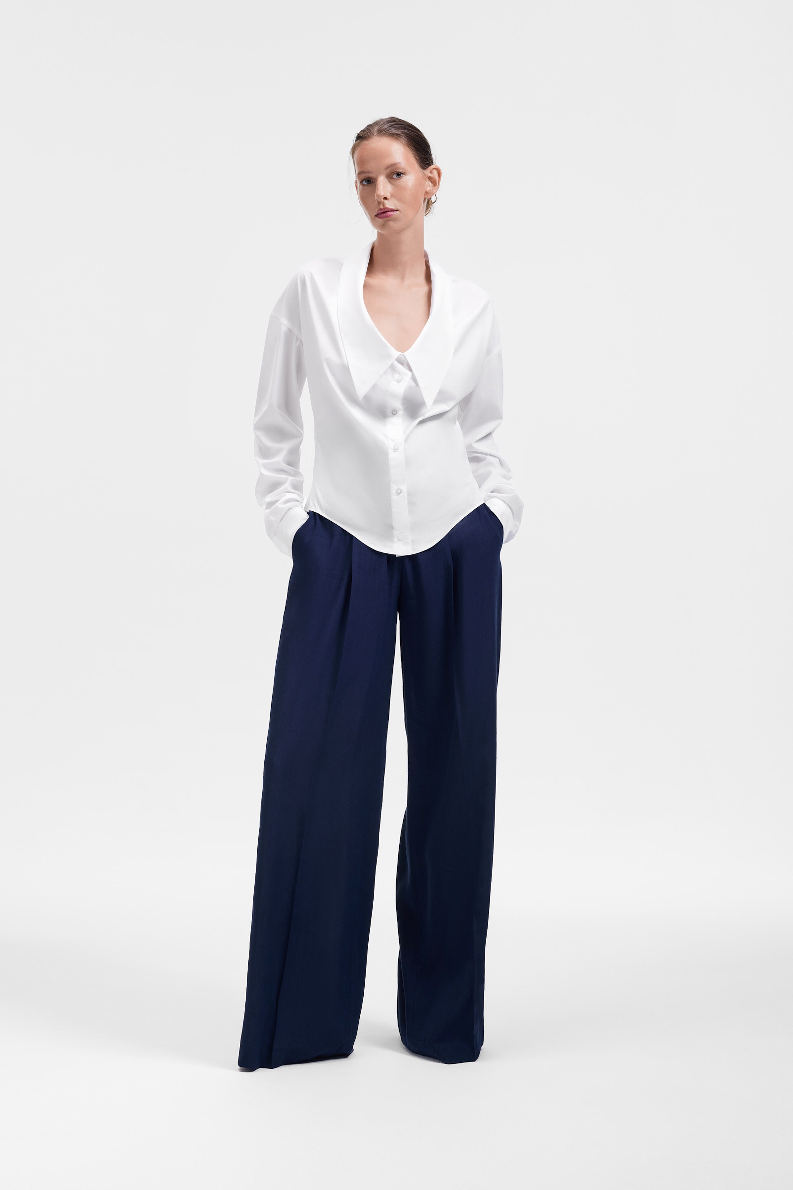 Woman wearing a white blouse and navy pants on a white background
