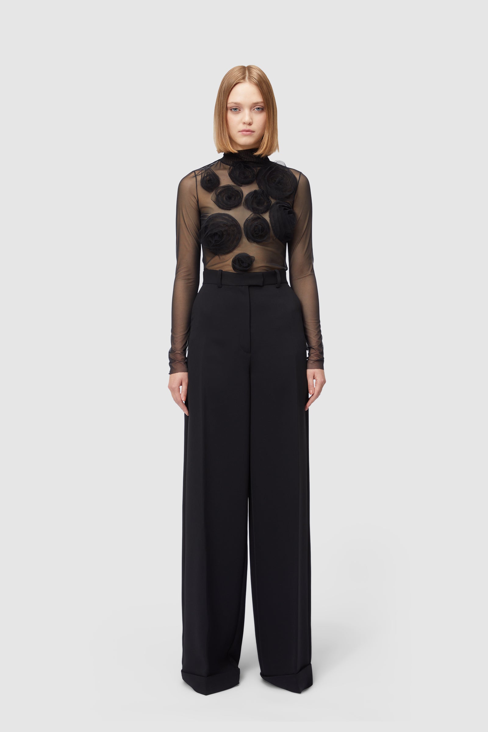 Elegant black sheer top with floral appliqué paired with high-waisted wide-leg trousers in sleek black fabric.