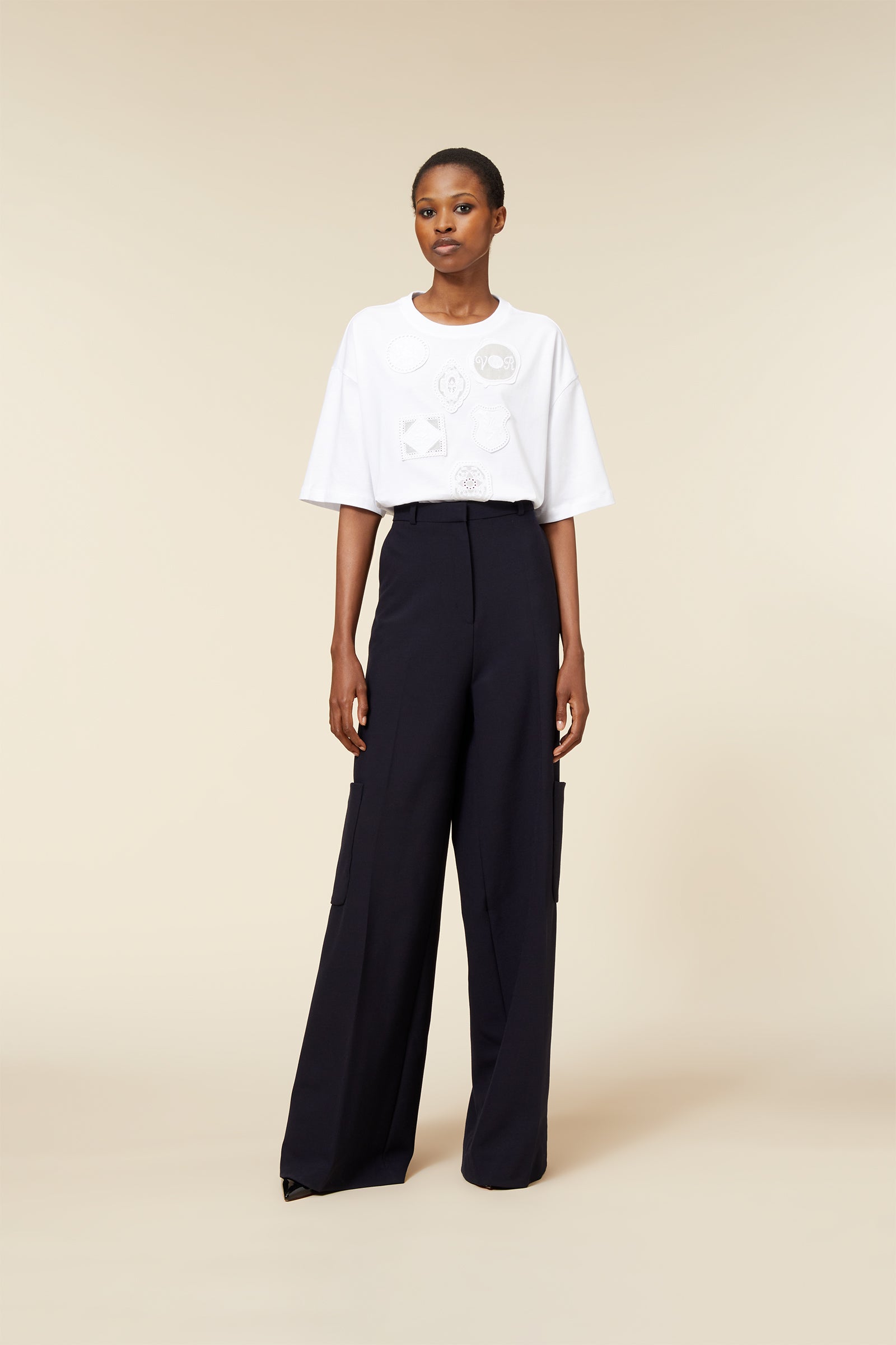 Wide-legged navy trousers with side pockets paired with a loose-fitting white T-shirt featuring intricate geometric embroidery.