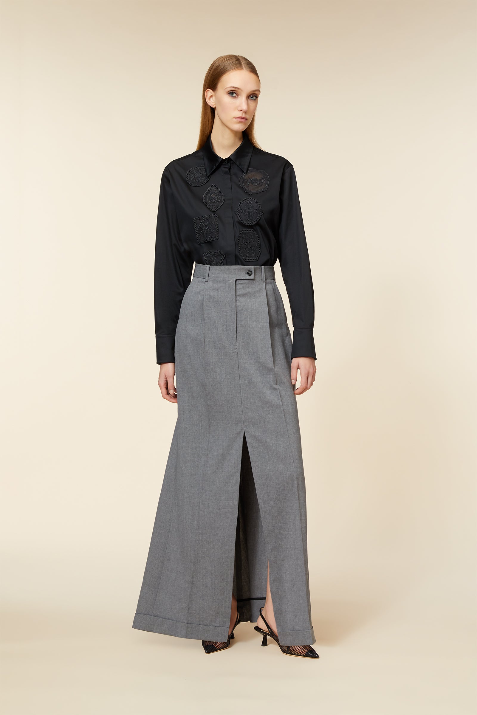 Elegant gray high-waisted maxi skirt with front slit paired with a black long-sleeve blouse featuring floral embroidery.