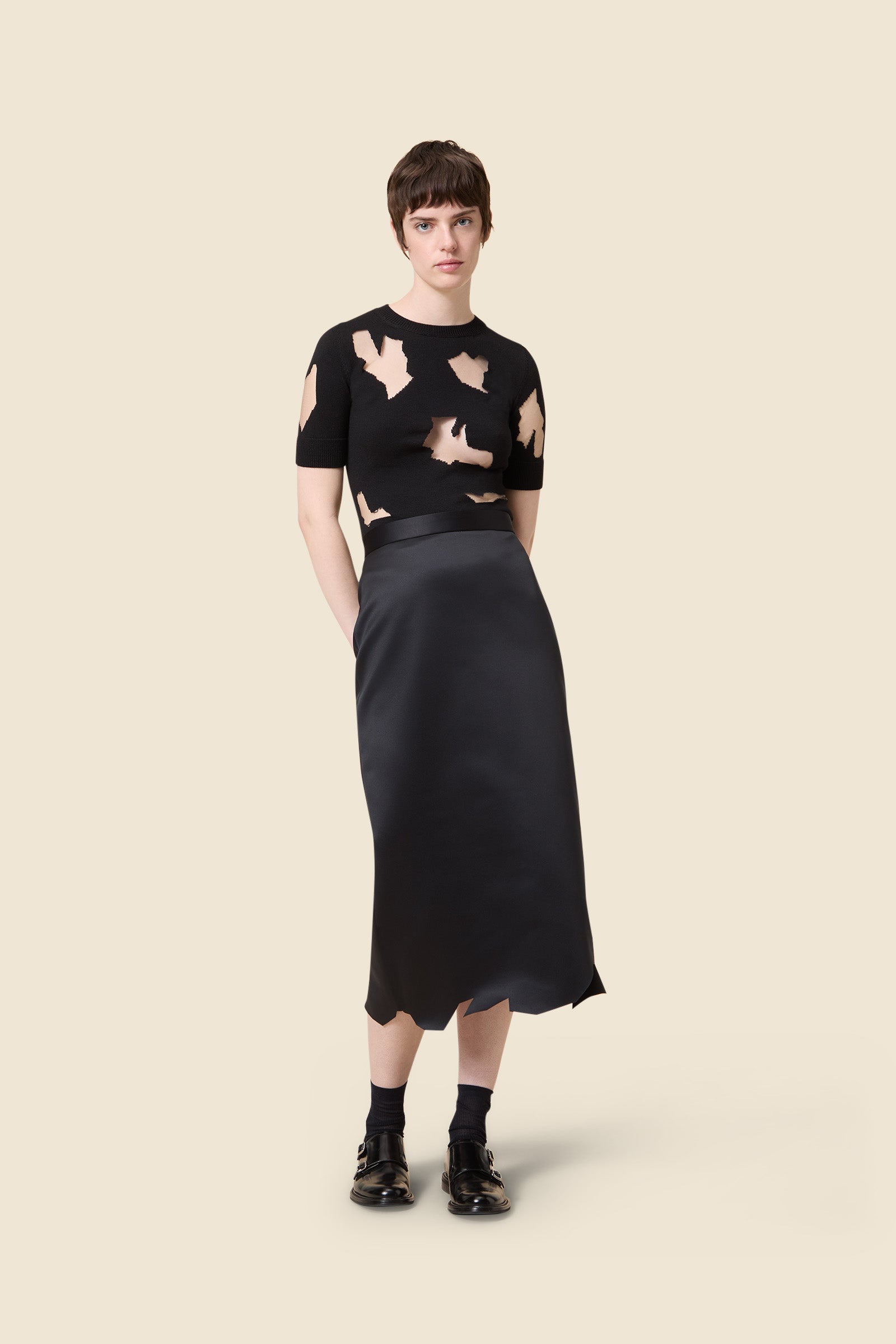 A black short-sleeved top with beige abstract cutouts, paired with a sleek, high-waisted black satin midi skirt.