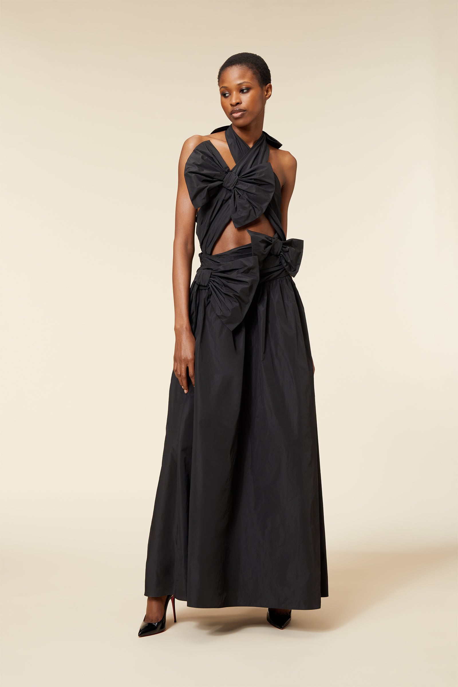 Elegant long black dress with large bows and halter neckline, highlighting a chic, sophisticated fashion style.