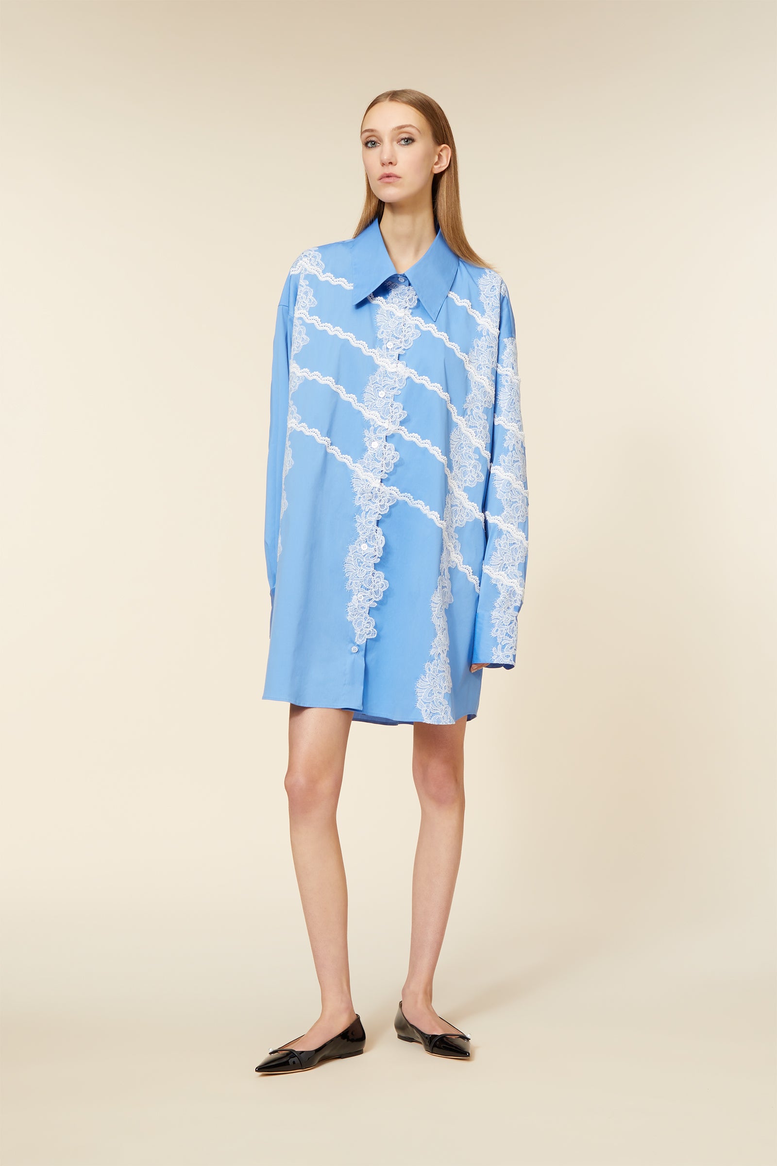 Oversized blue shirt dress adorned with intricate white lace detailing in diagonal stripes, paired with black pointed flats.