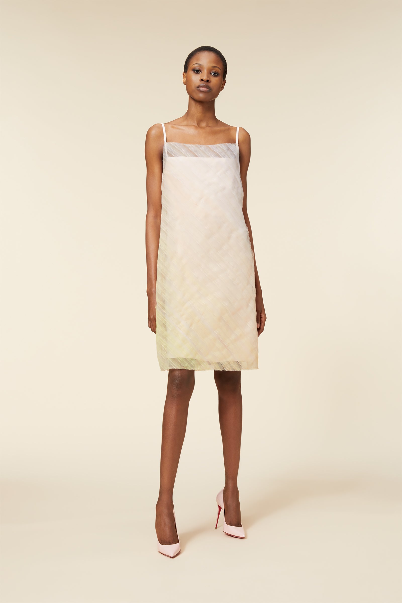 Model wearing a light pastel-colored, sleeveless dress with thin straps and subtle geometric patterns.