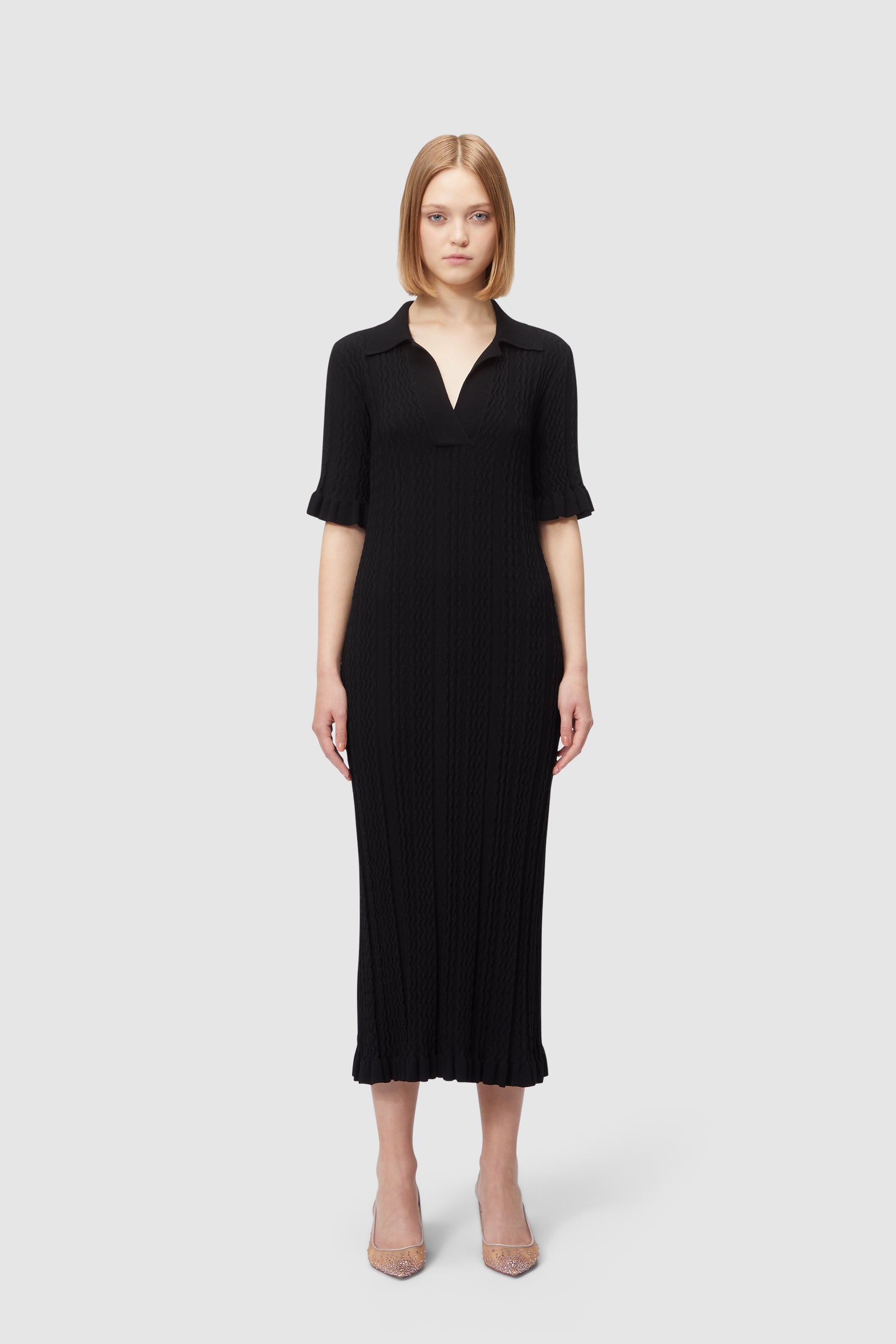 Woman wearing an elegant black knit V-neck midi dress with half sleeves and ruffled hem against plain background.