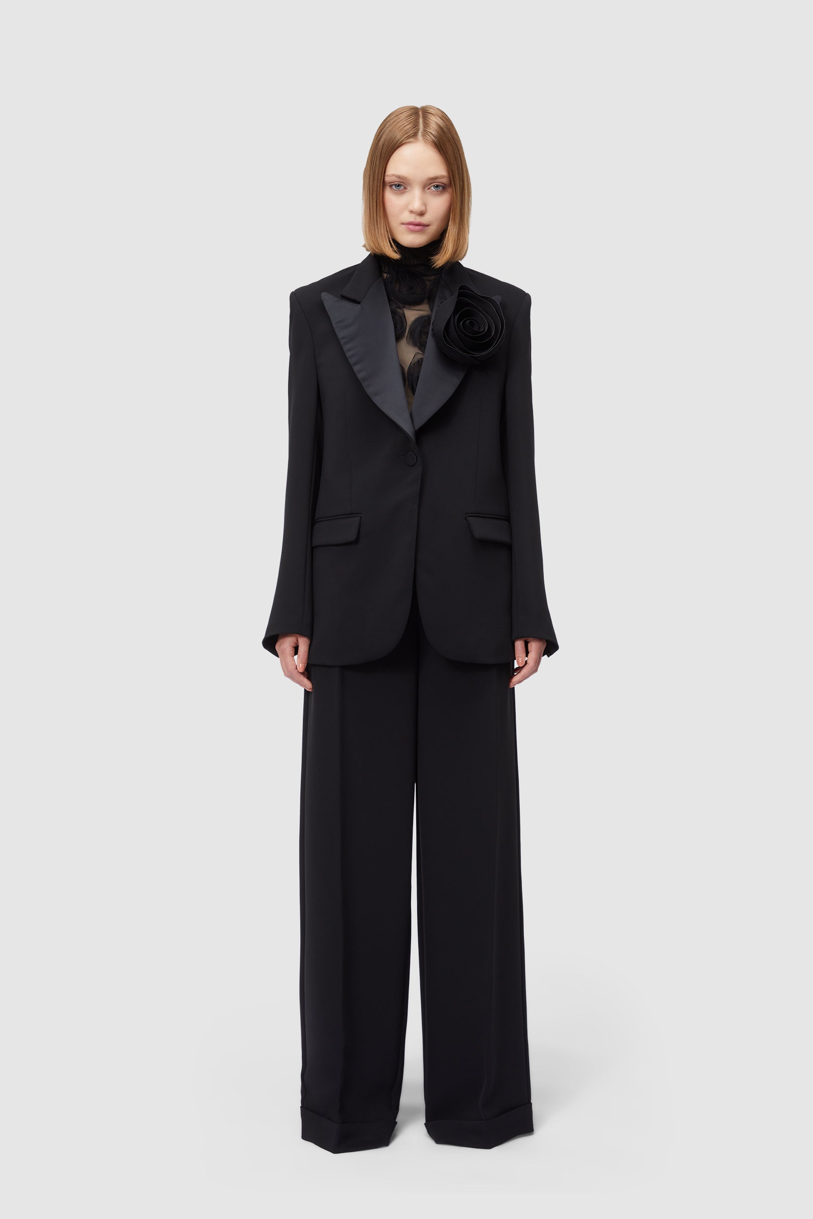 Elegant black blazer with satin lapels and a large floral detail, paired with wide-legged matching black trousers.