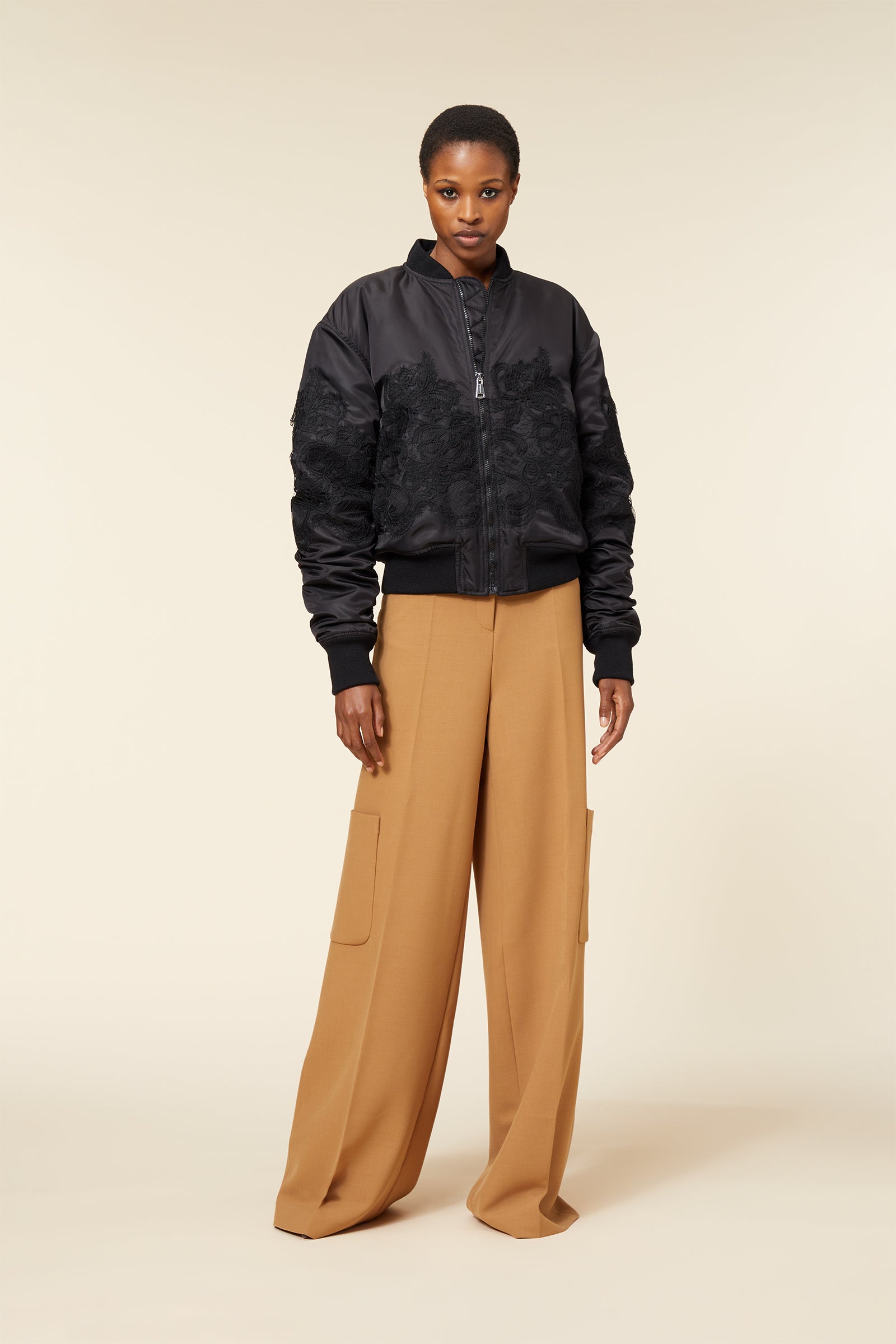 Black bomber jacket with intricate lace detailing teamed with wide-leg camel cargo pants for a modern chic look.