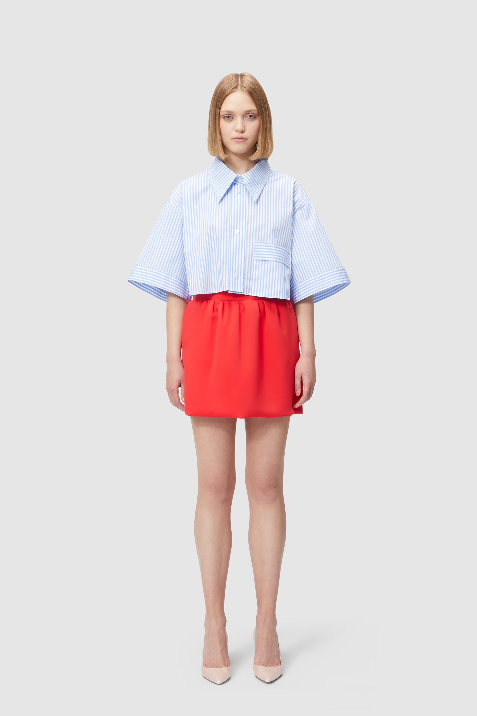 A blue striped oversize shirt paired with a vibrant red skirt, creating a striking contrast and modern look.