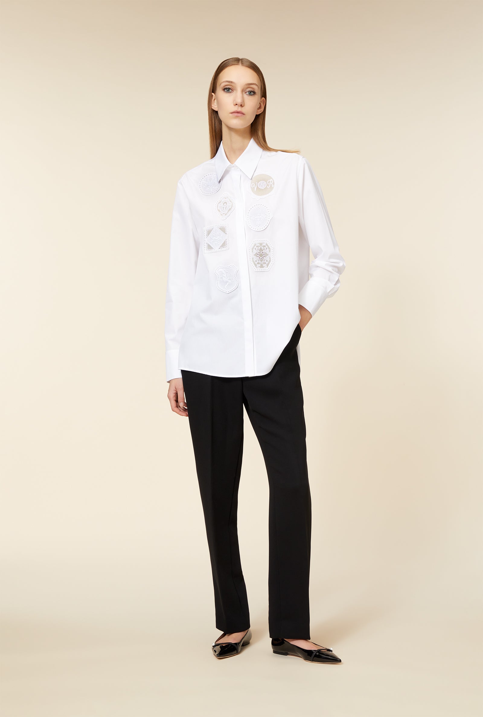 Elegant wide-collared white blouse with intricate lace patches, paired with sleek black tailored trousers and black shoes.