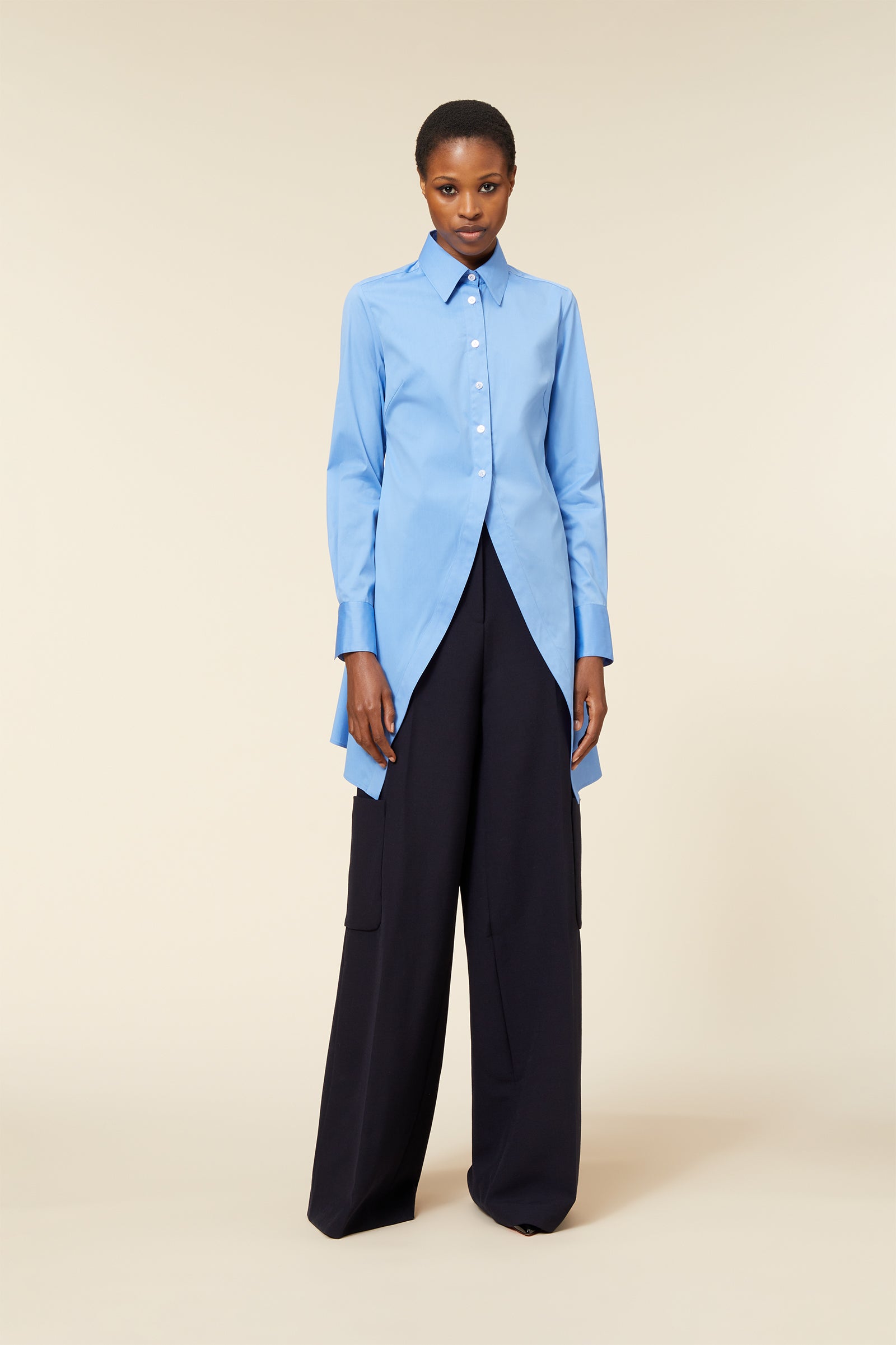 Elegant blue cotton blouse with asymmetrical hem paired with sleek black wide-leg trousers on a neutral background.