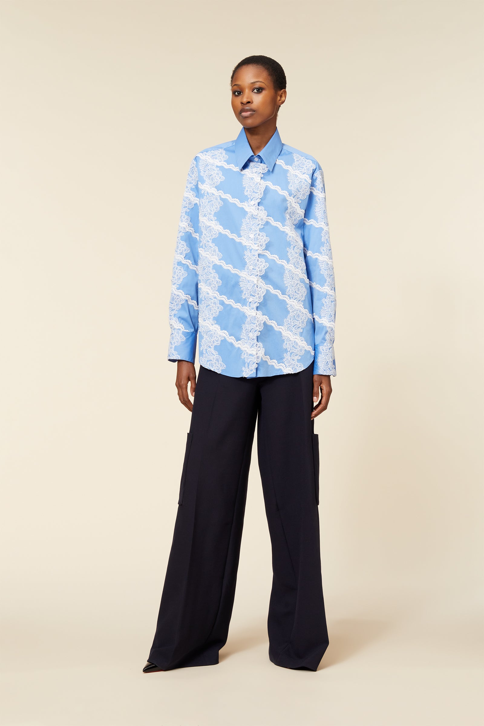 The shirt features intricate white lace patterns on a light blue base paired with sleek black wide-leg trousers.