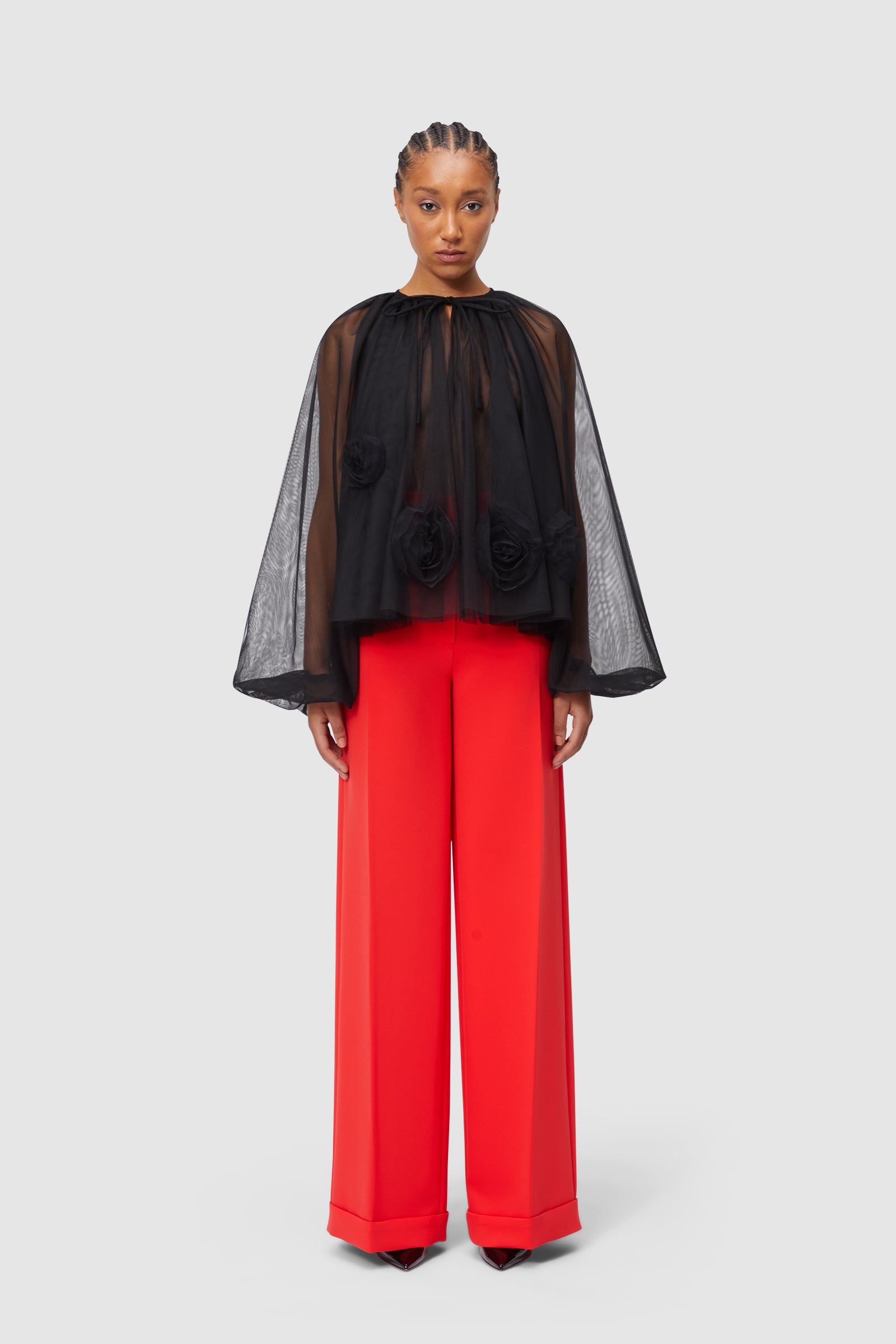 Sheer black blouse with floral appliqués paired with vibrant red wide-leg trousers for a bold, stylish statement.