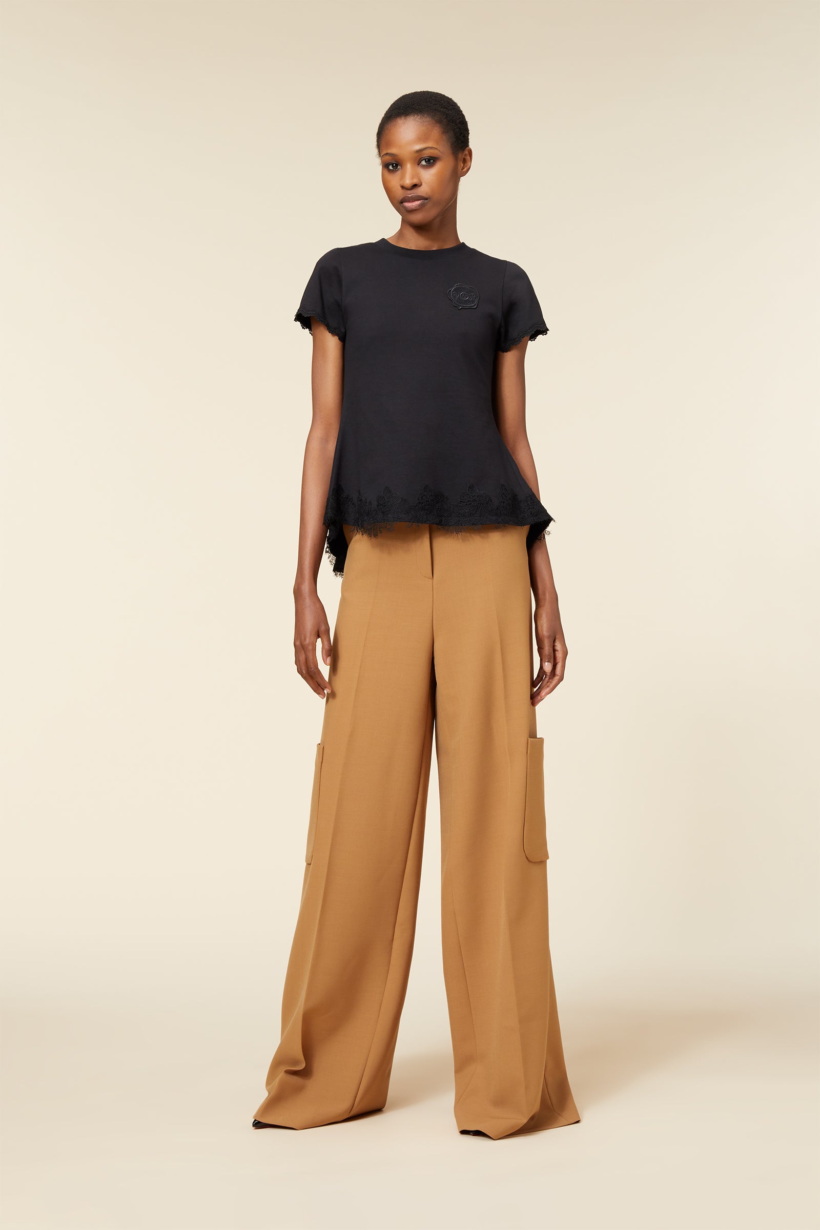 Black top with subtle floral embroidery paired with wide-legged camel pants featuring large side pockets, against a neutral backdrop.