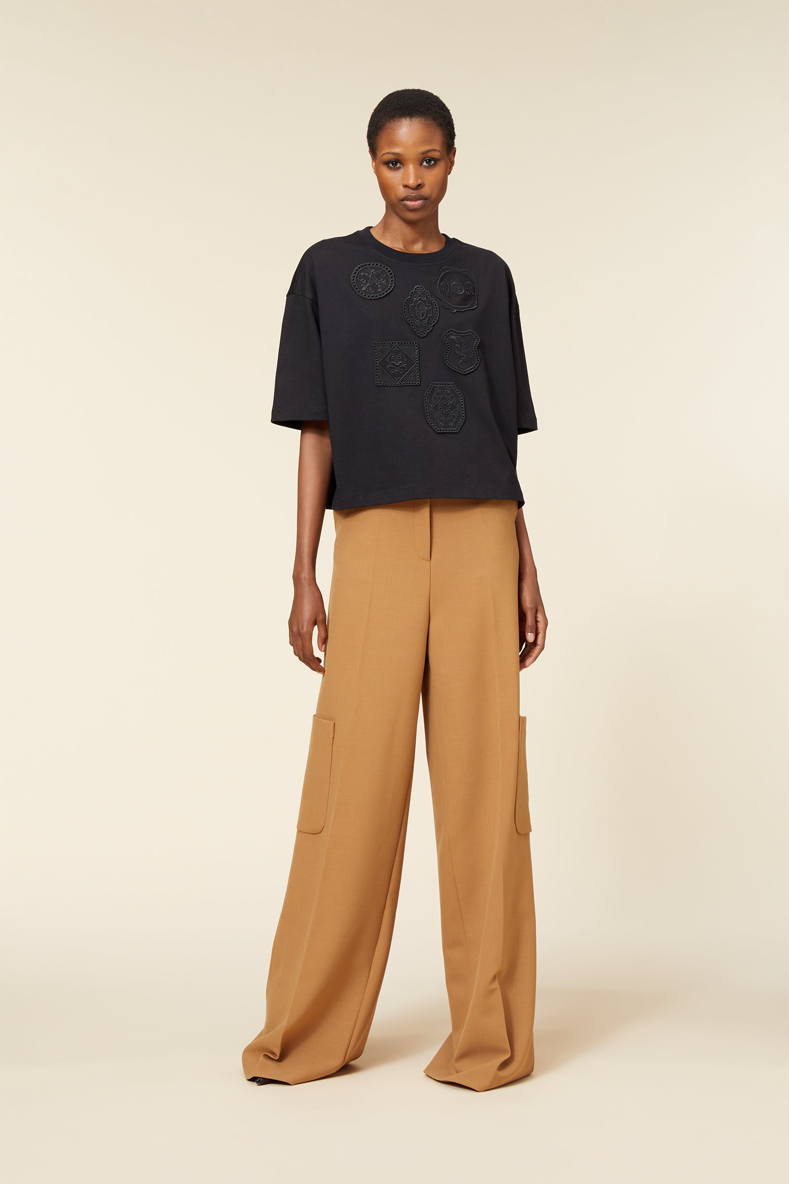 Black oversized t-shirt with embossed motifs paired with high-waisted camel wide-leg trousers featuring large pockets.