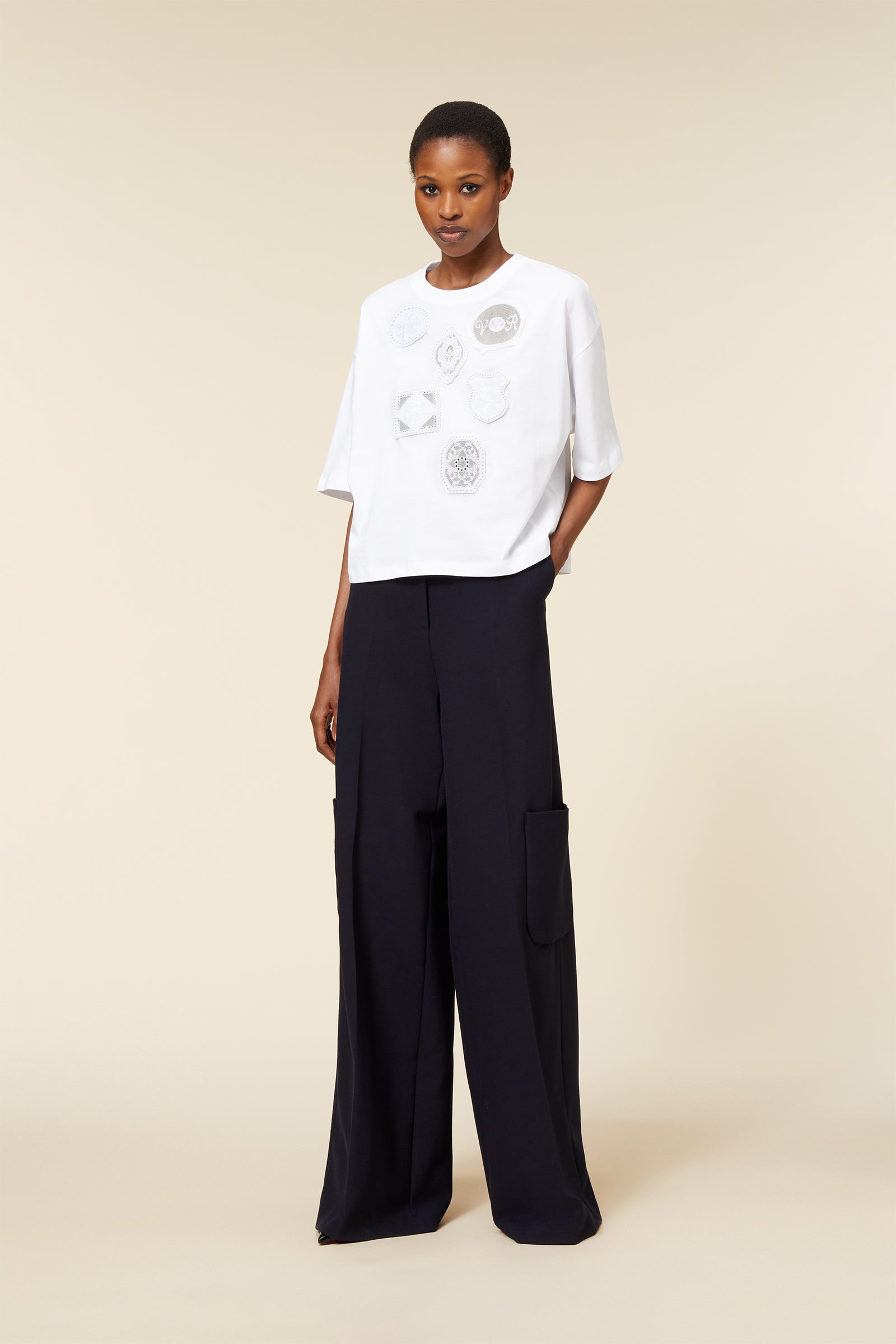 Loose-fit white top with intricate embroidered patches, paired with high-waist wide-leg black trousers featuring side pockets.