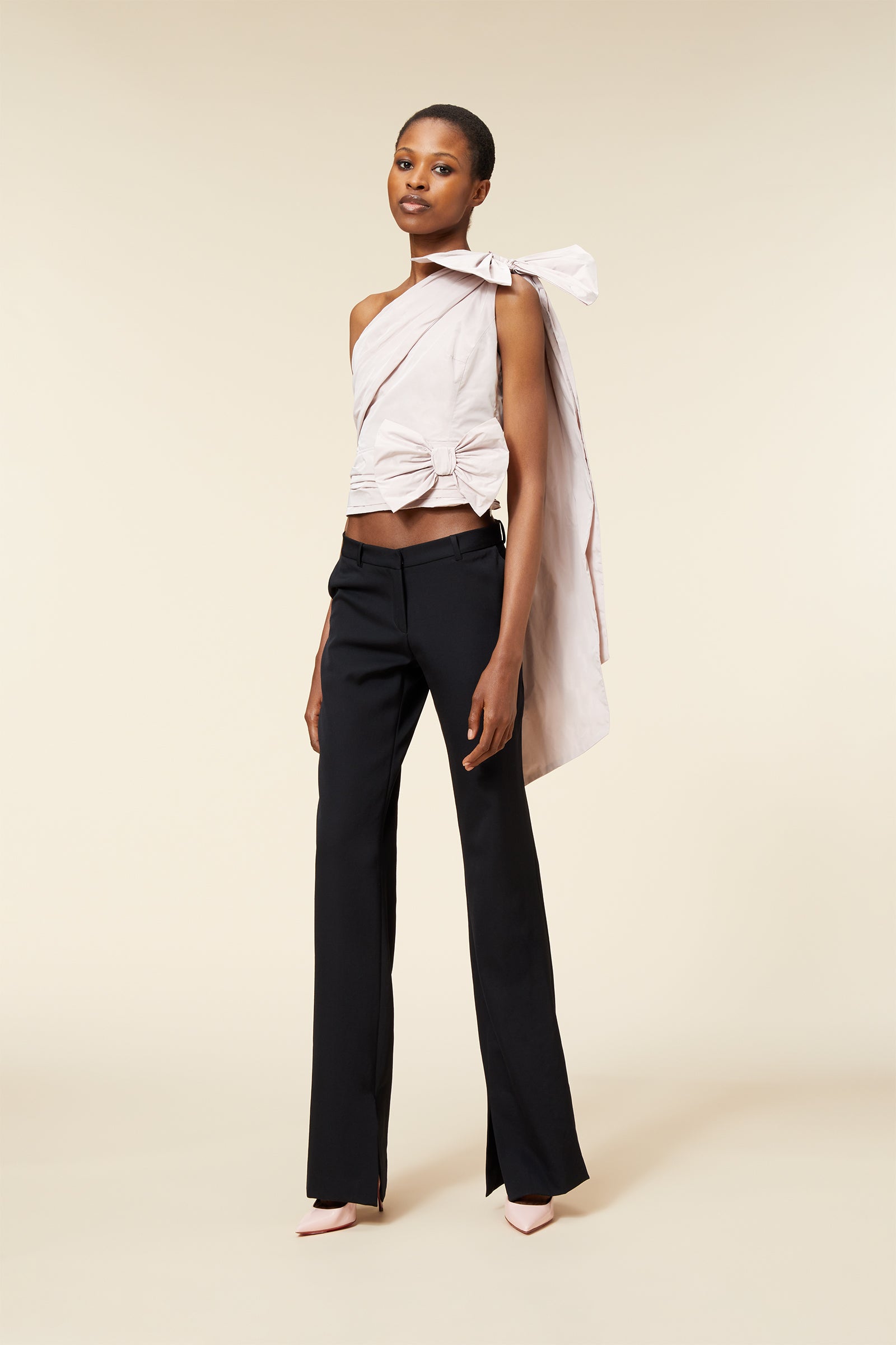 Elegant woman wearing a sophisticated, asymmetrical white top with bow detail paired with classic black trousers.