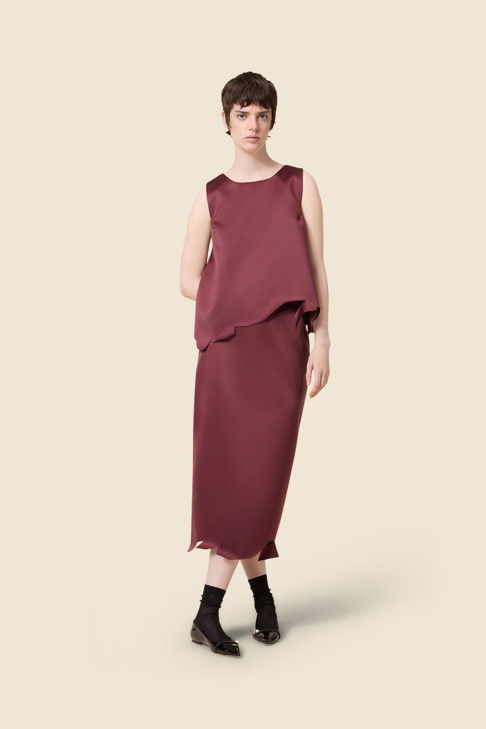 Sleek burgundy sleeveless dress with asymmetrical hem, elegantly crafted in satin fabric, showcasing minimalist chic style.