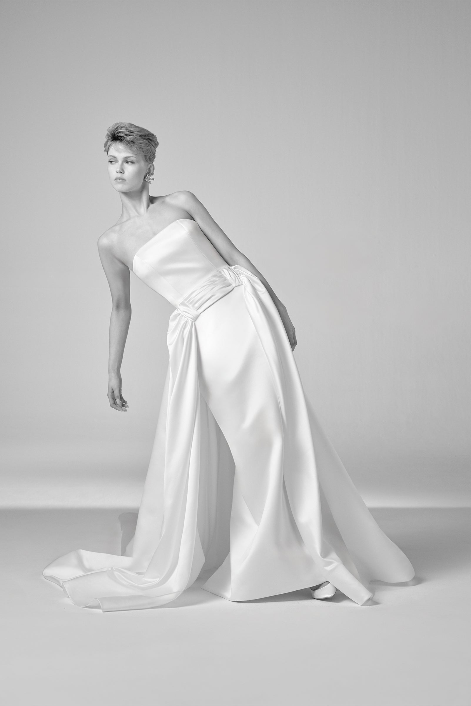 This elegant gown showcases a sleek bonded satin column skirt beneath a gracefully draped layer, knotted at the waist for a refined touch, from the Viktor&Rolf Mariage collection.