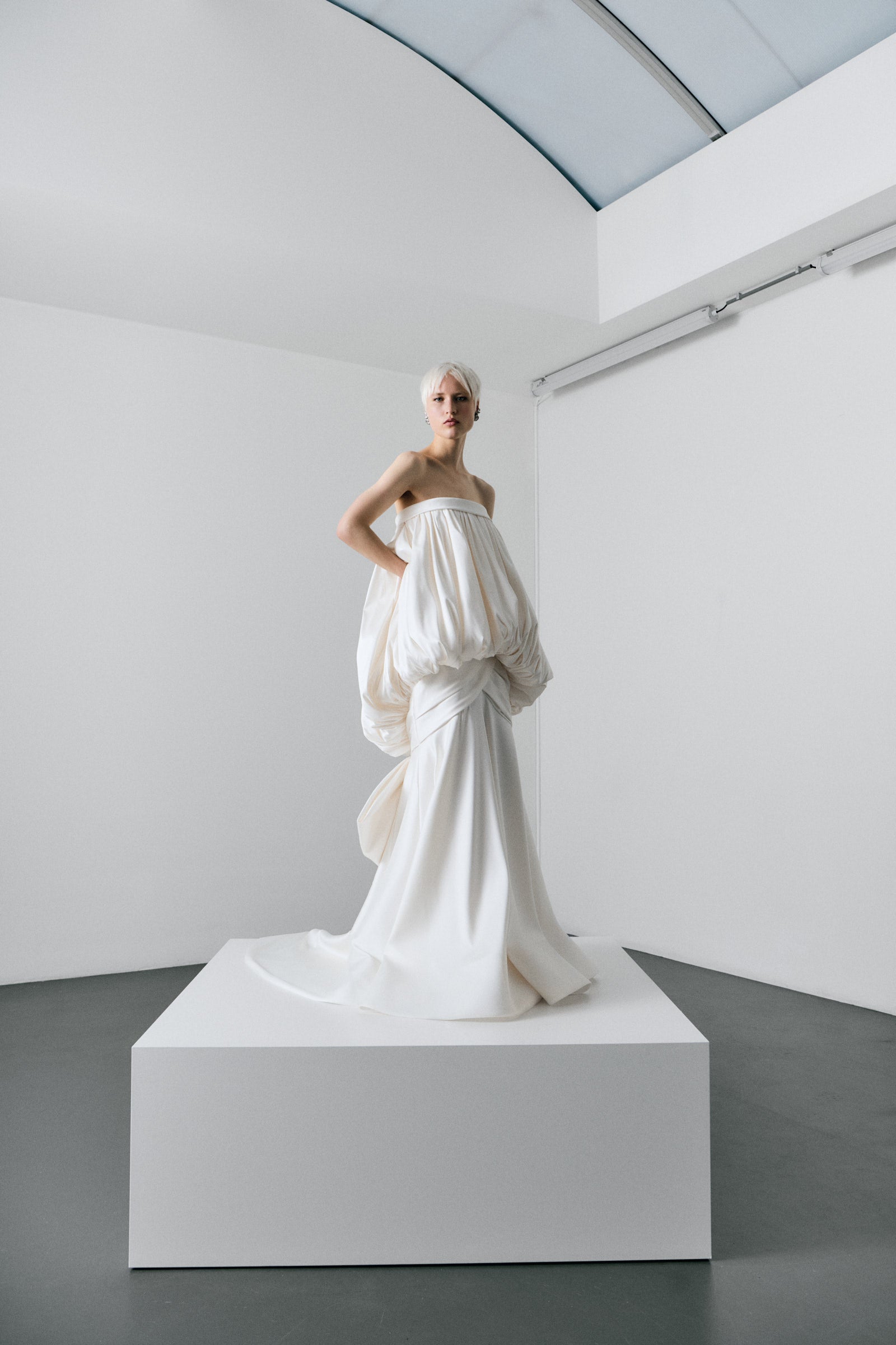 White sculpture of a draped garment on a pedestal in a minimalistic setting