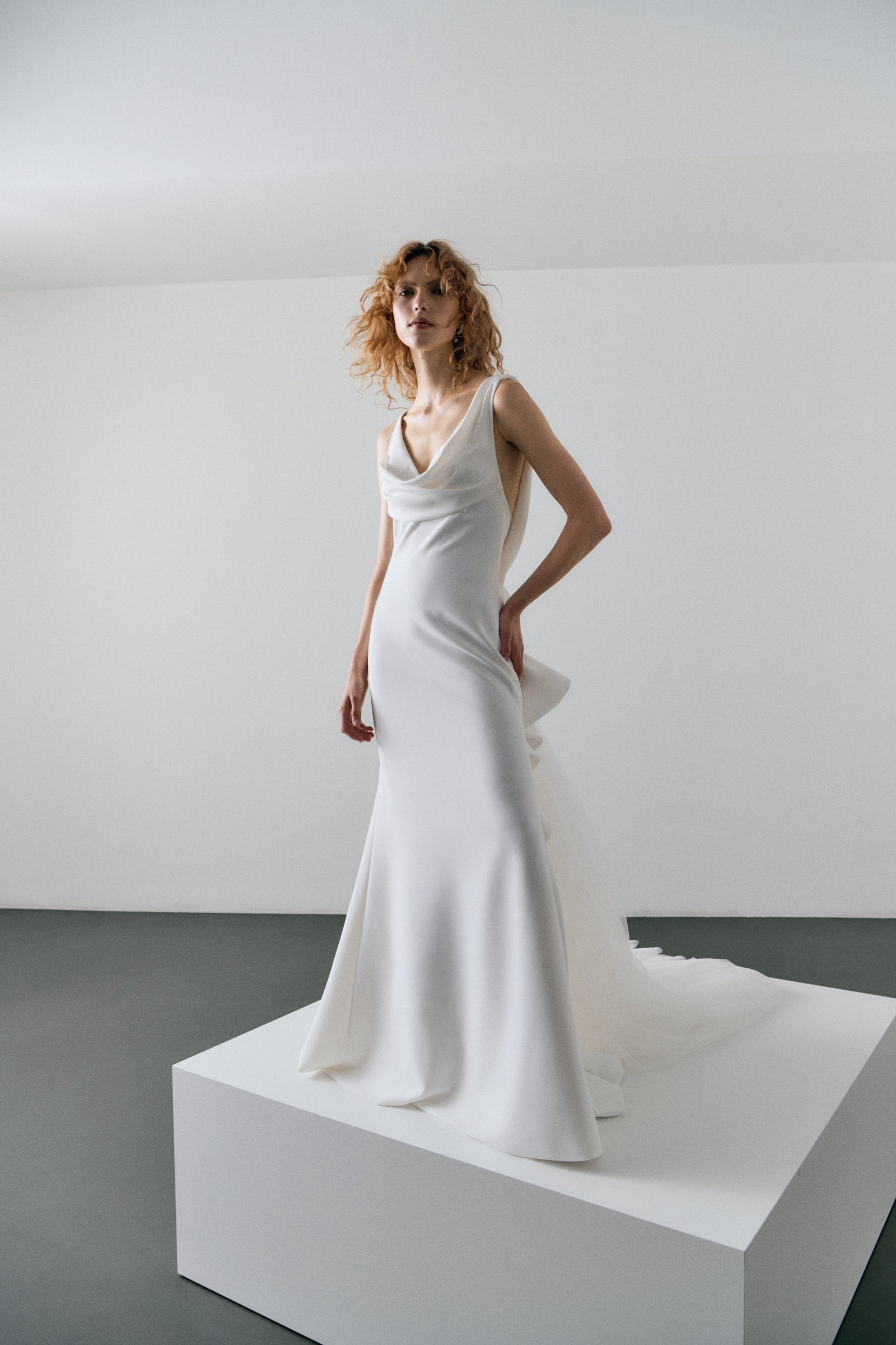 Woman in a white wedding dress standing on a white platform against a plain background