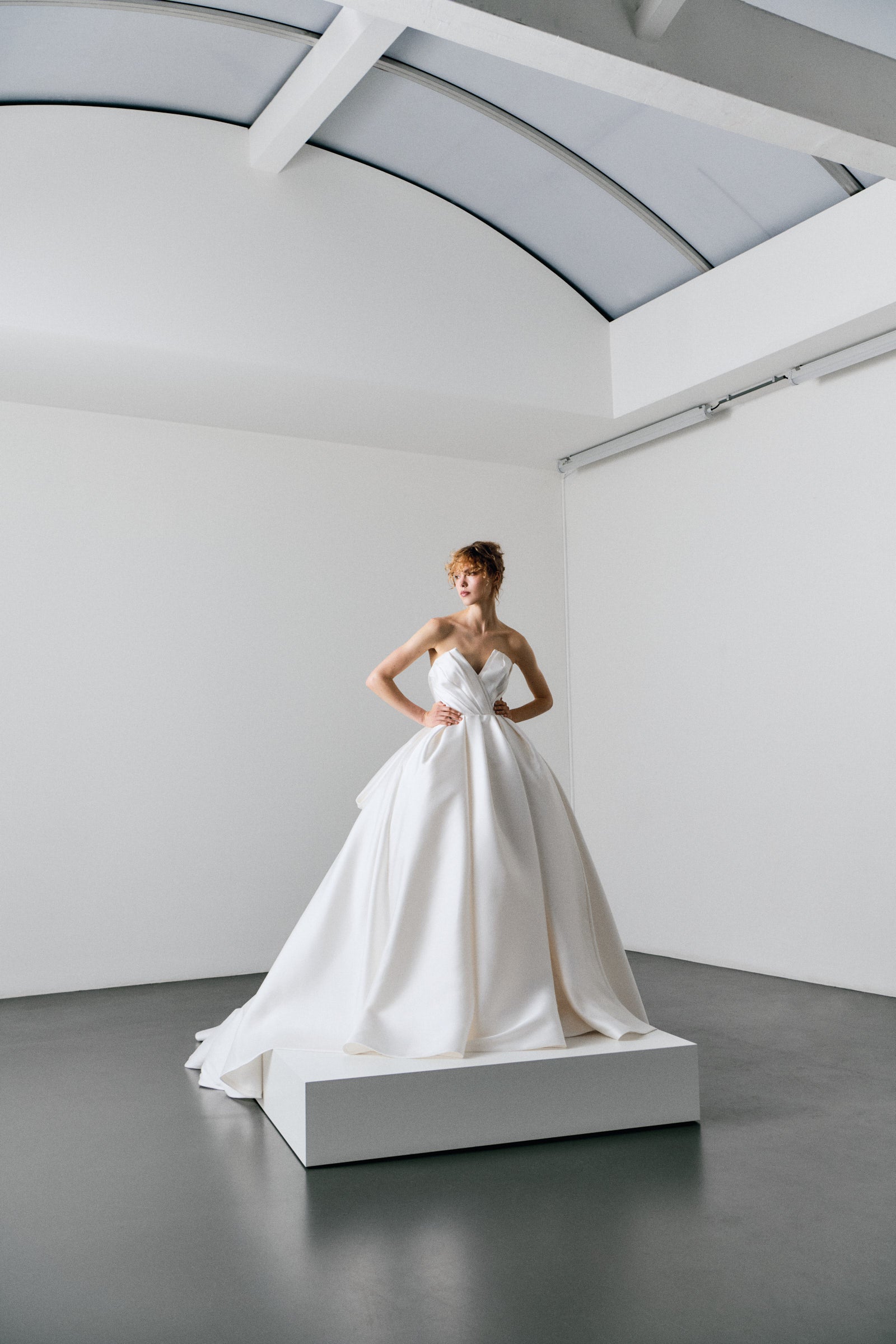 Woman in a white wedding dress standing on a platform in a minimalistic room.