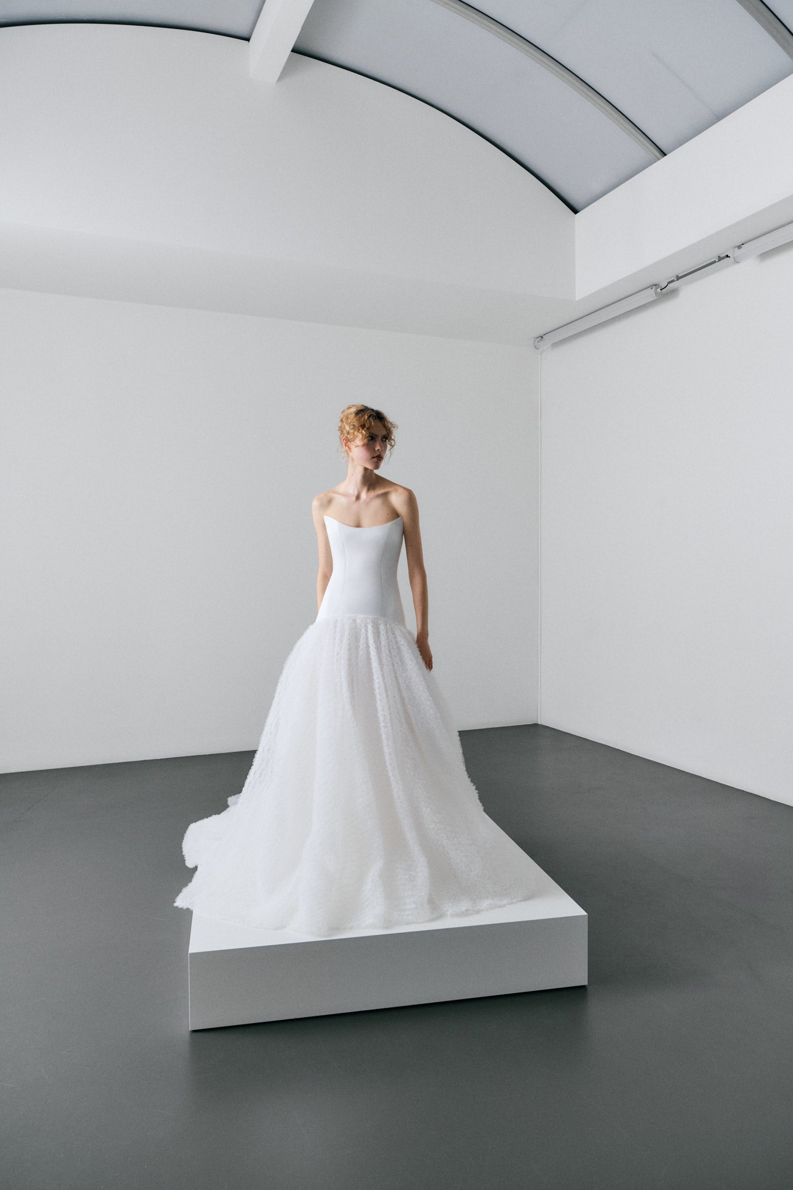 White wedding dress on a mannequin in a minimalistic room with white walls and gray floor.