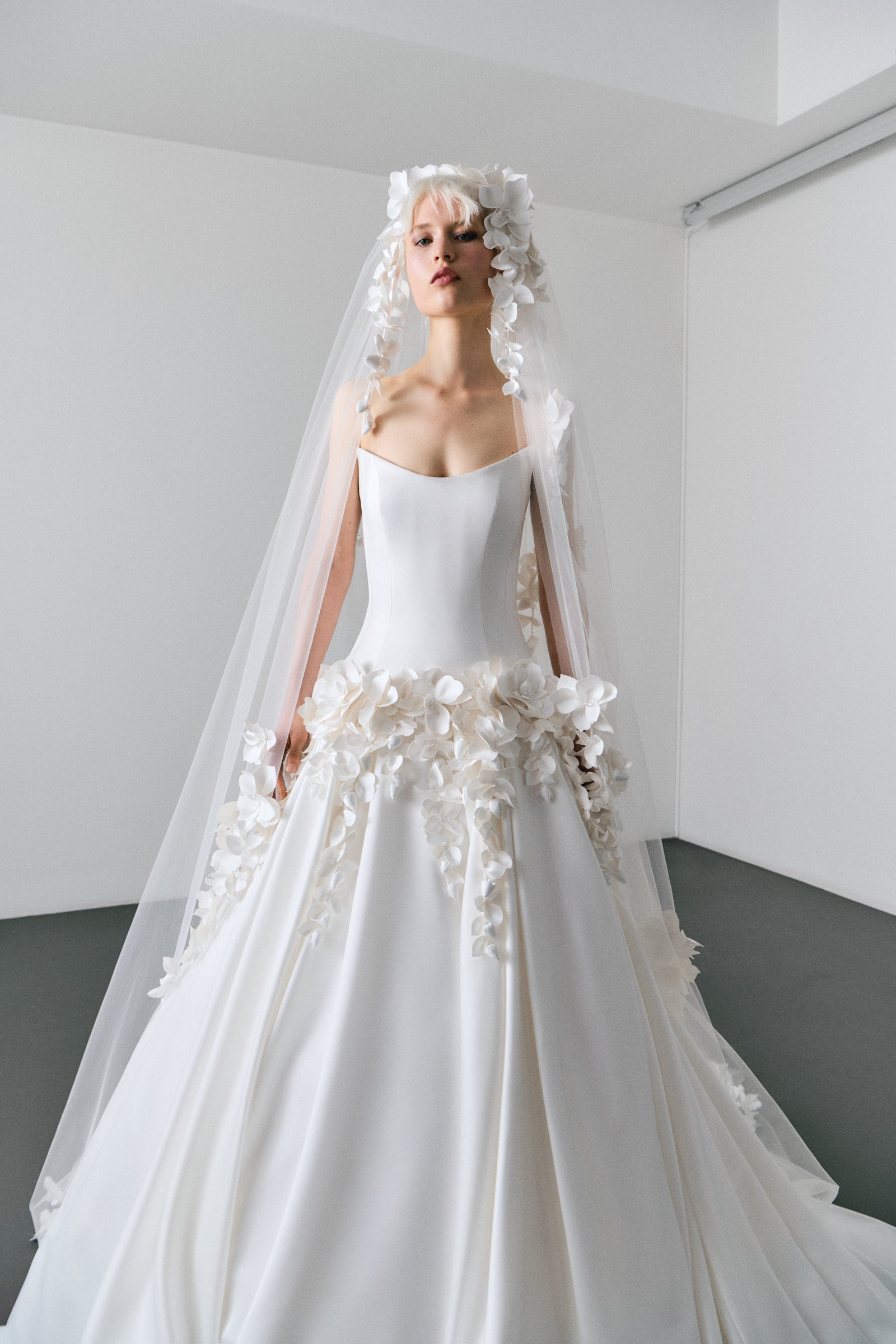 White wedding dress with floral details and a long veil on a plain background