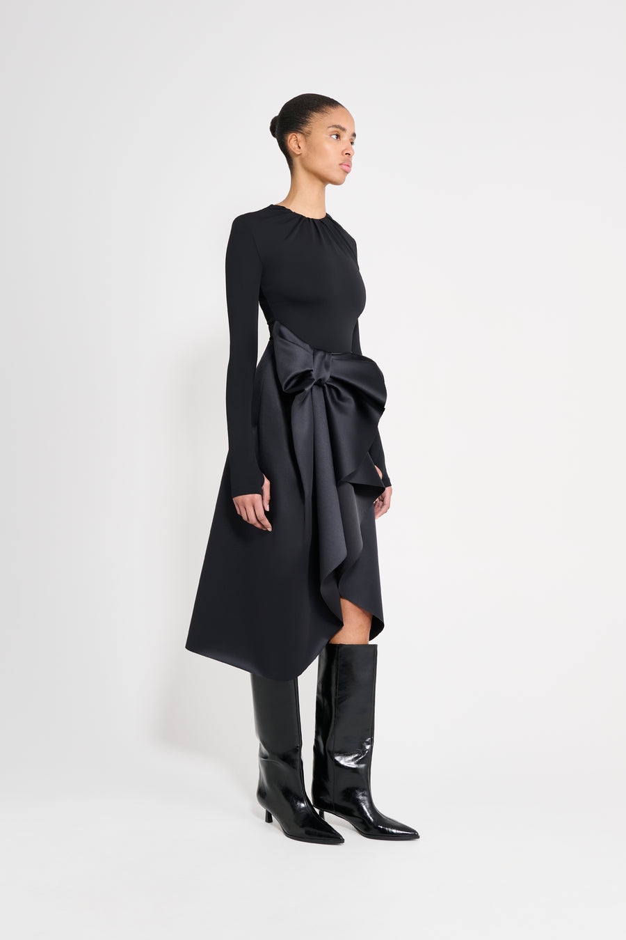 Model wearing a black satin skirt with a black long-sleeve top on a white background.