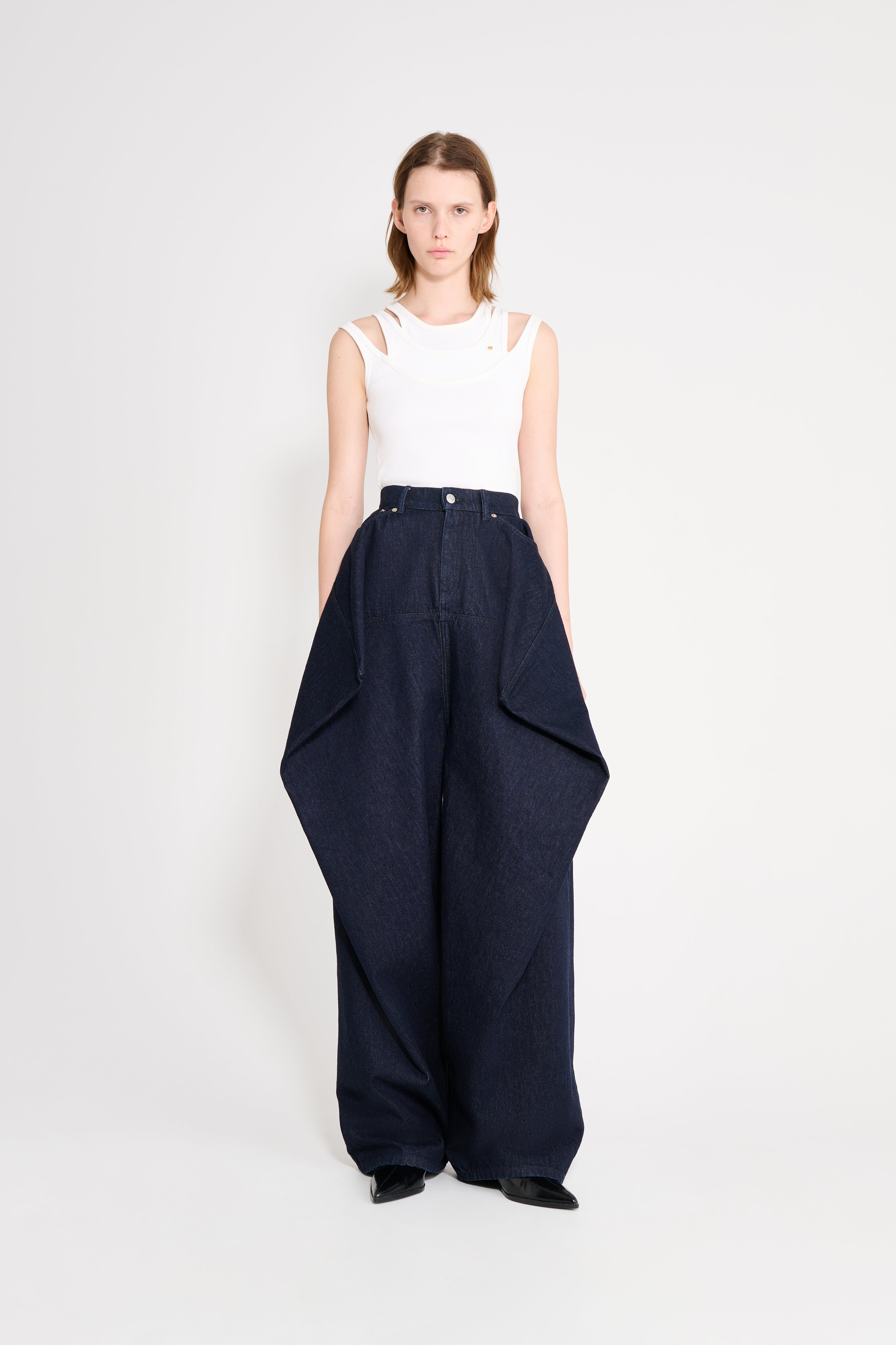 Woman wearing a white sleeveless top and dark blue wide-leg pants on a white background