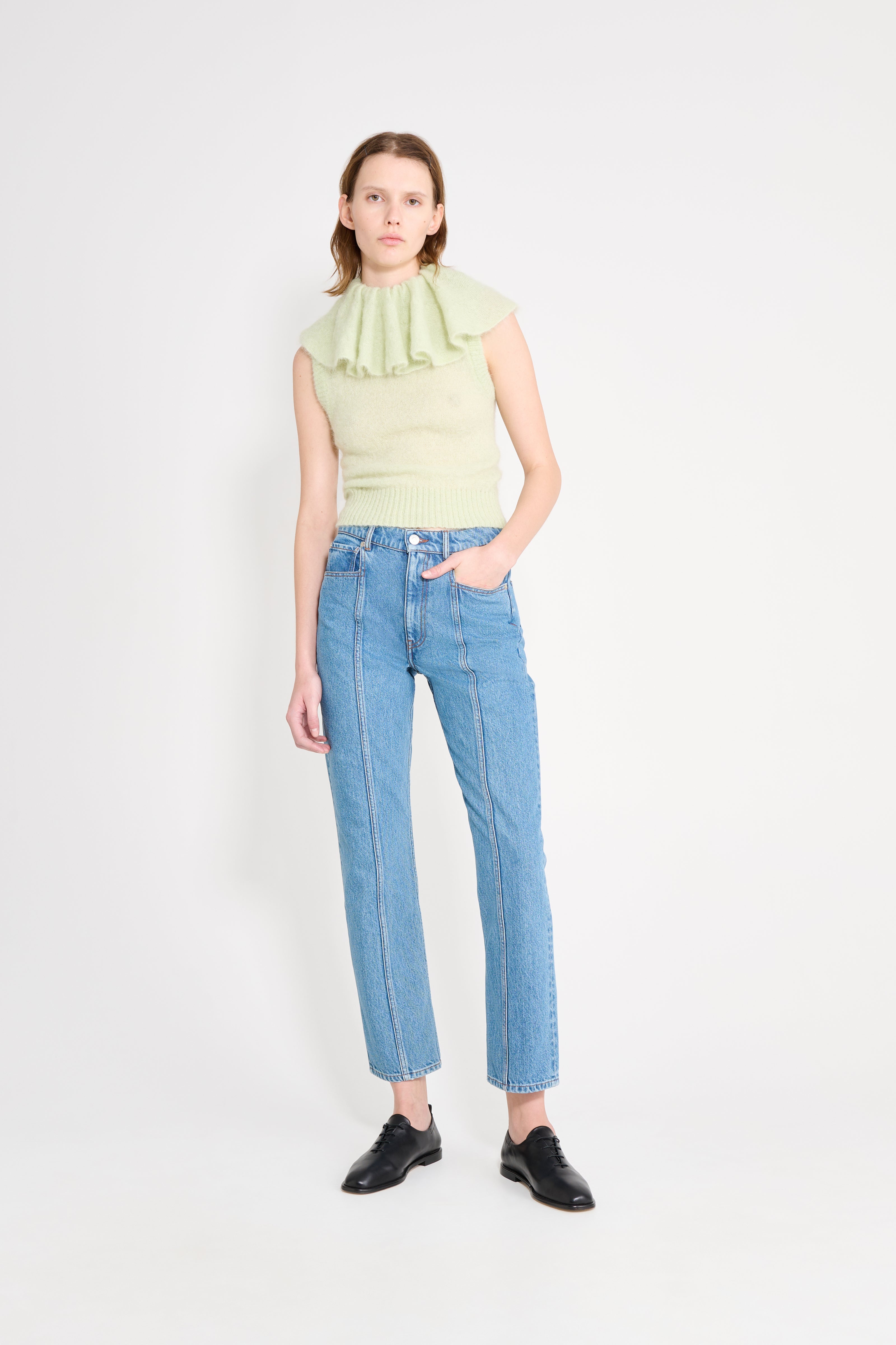 Woman wearing a light green sleeveless top and blue jeans on a white background