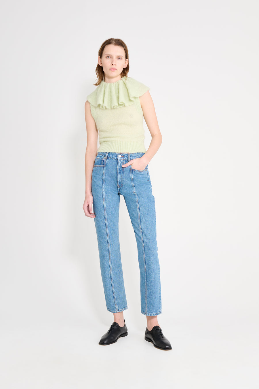 Woman wearing a light green sleeveless top and blue jeans on a white background