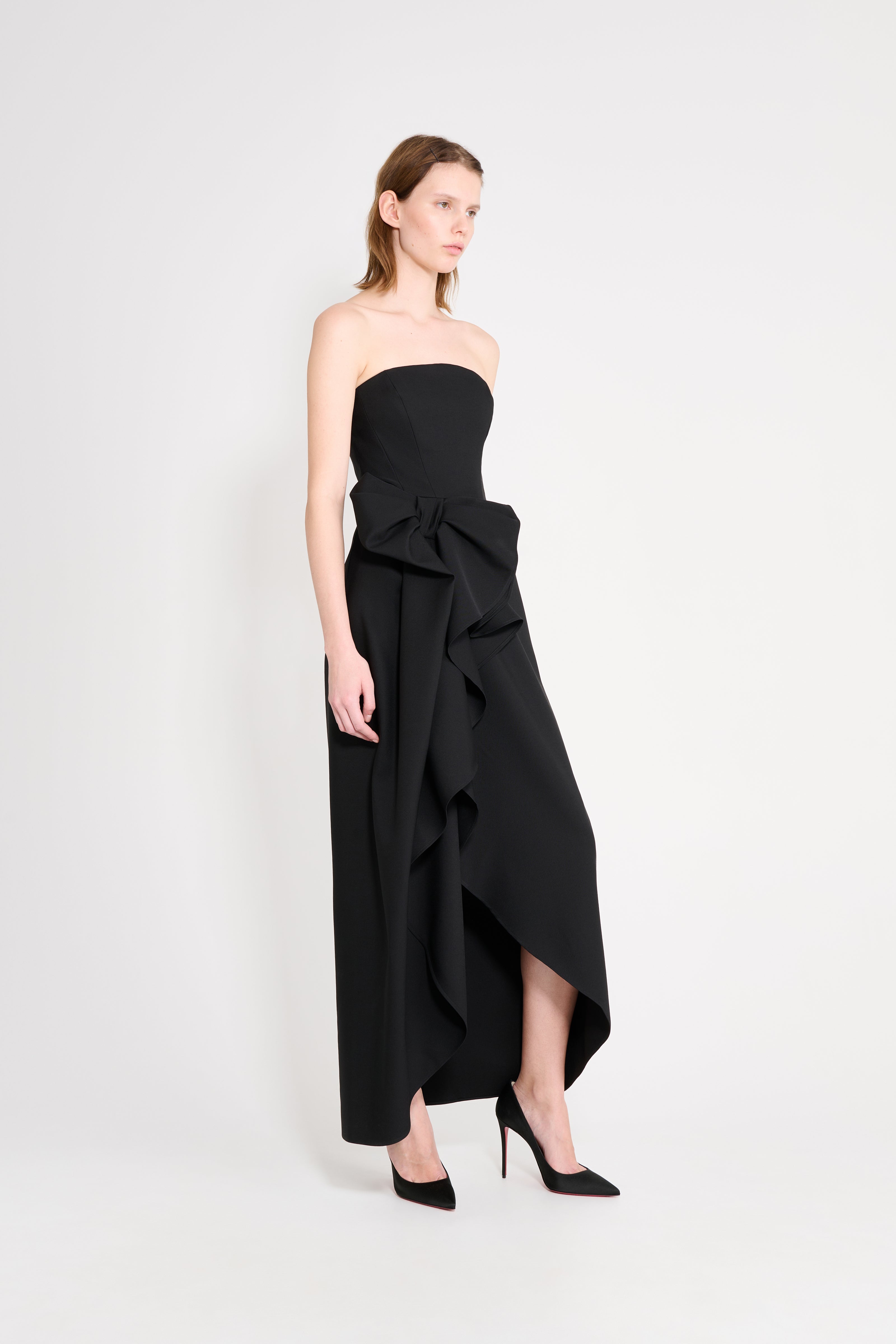 Woman wearing a black strapless dress with a large bow on a white background