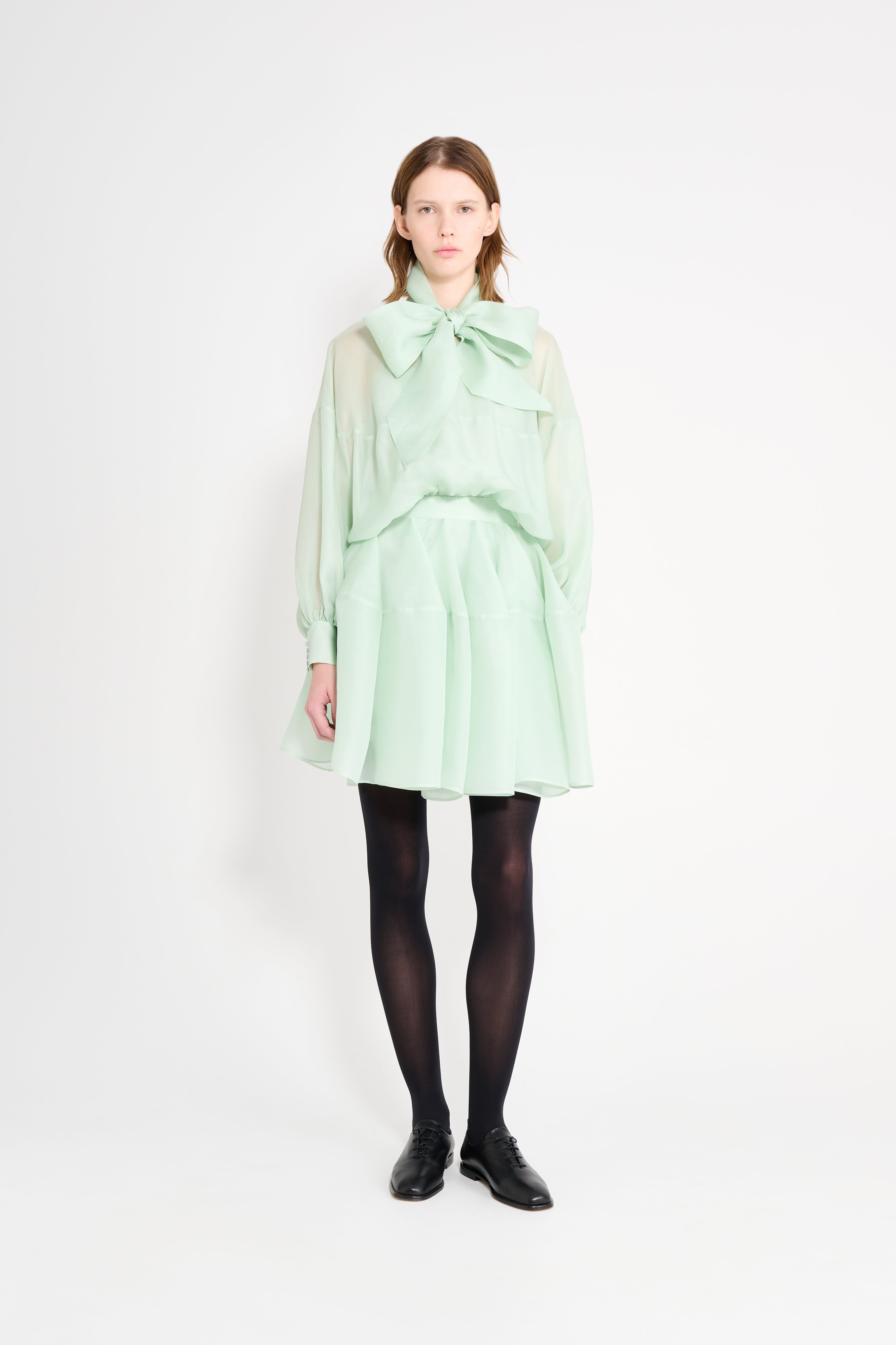 Person wearing a light green dress with a large bow on a white background