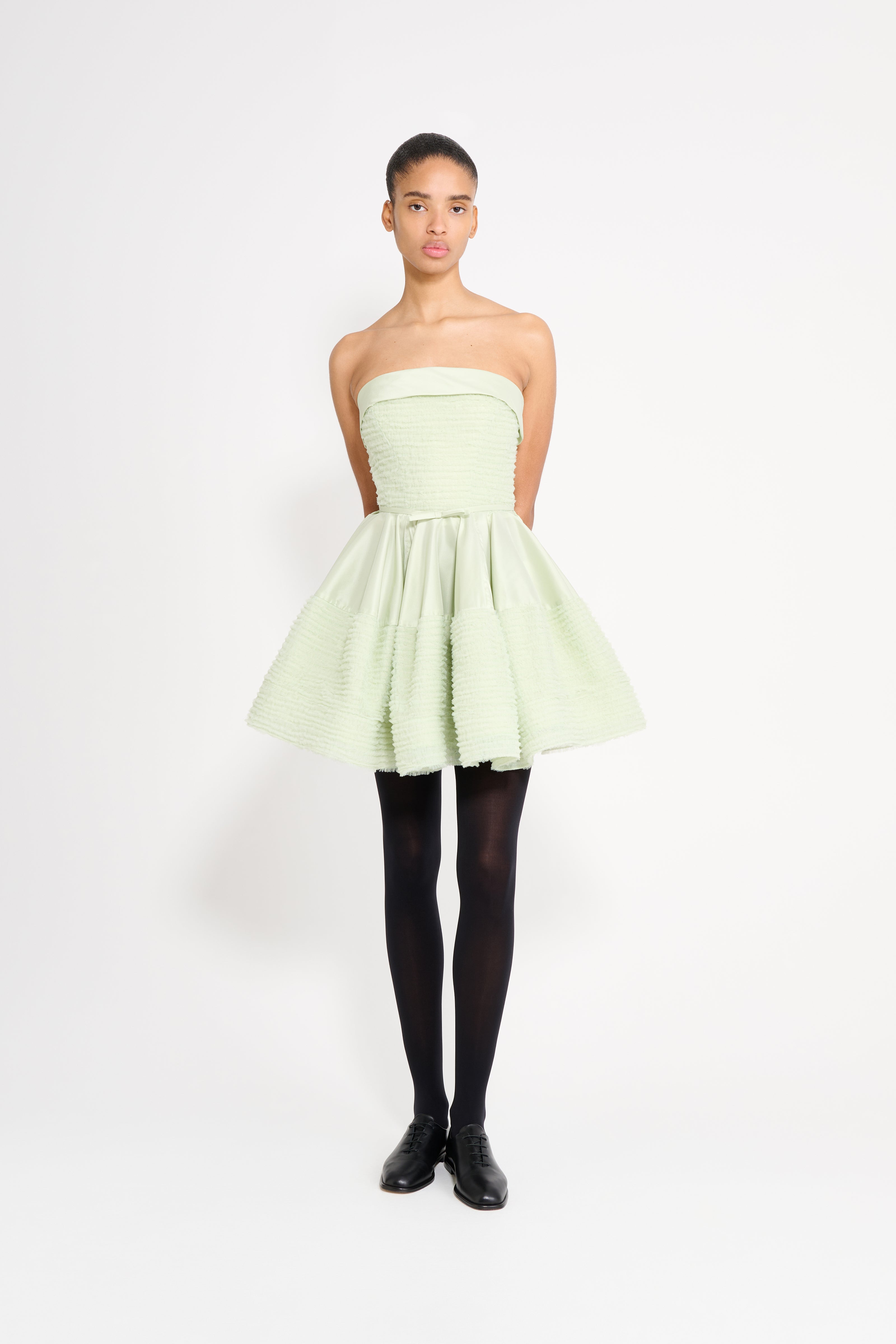 Woman wearing a light green strapless dress on a white background