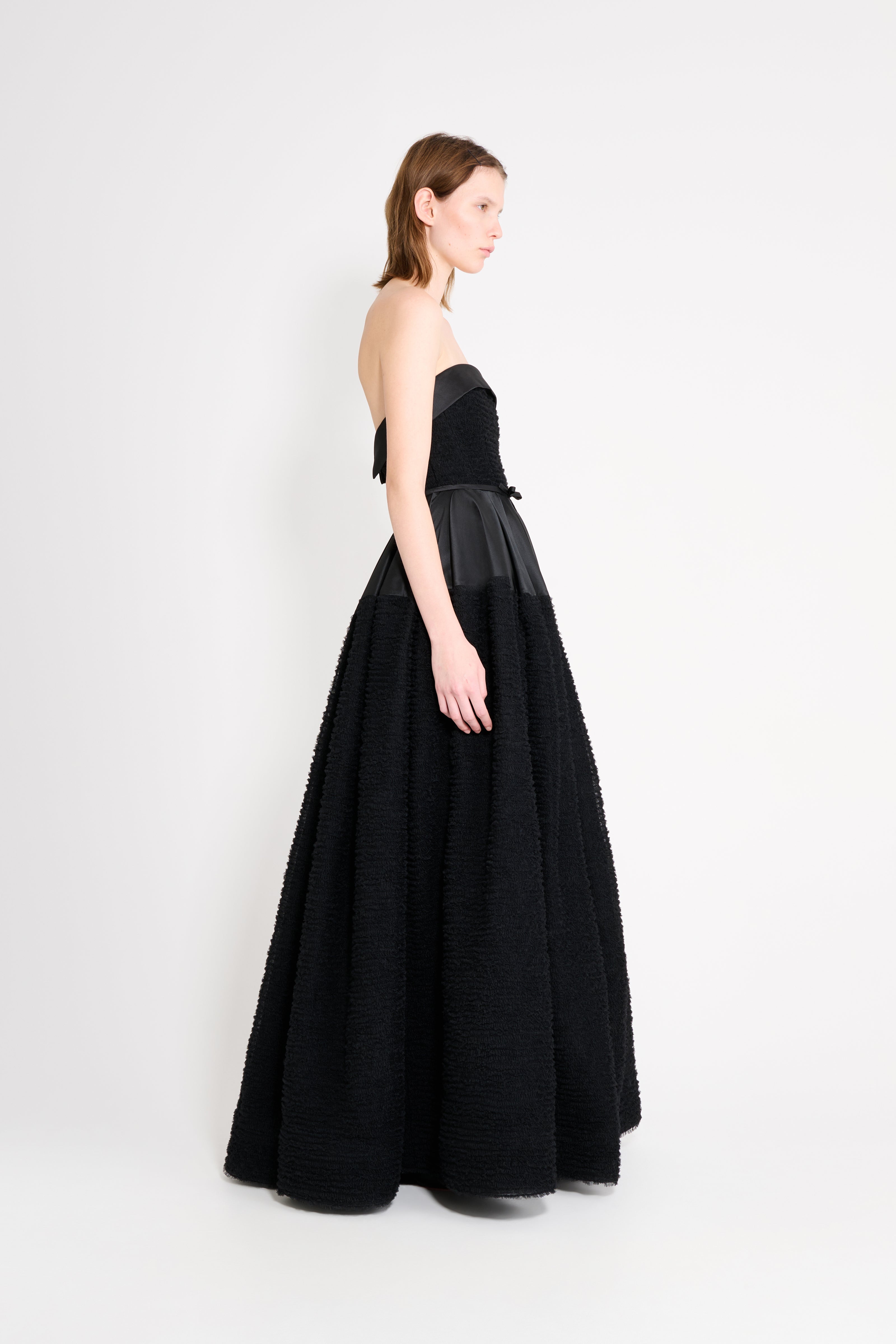 Model wearing a black strapless gown from the side.